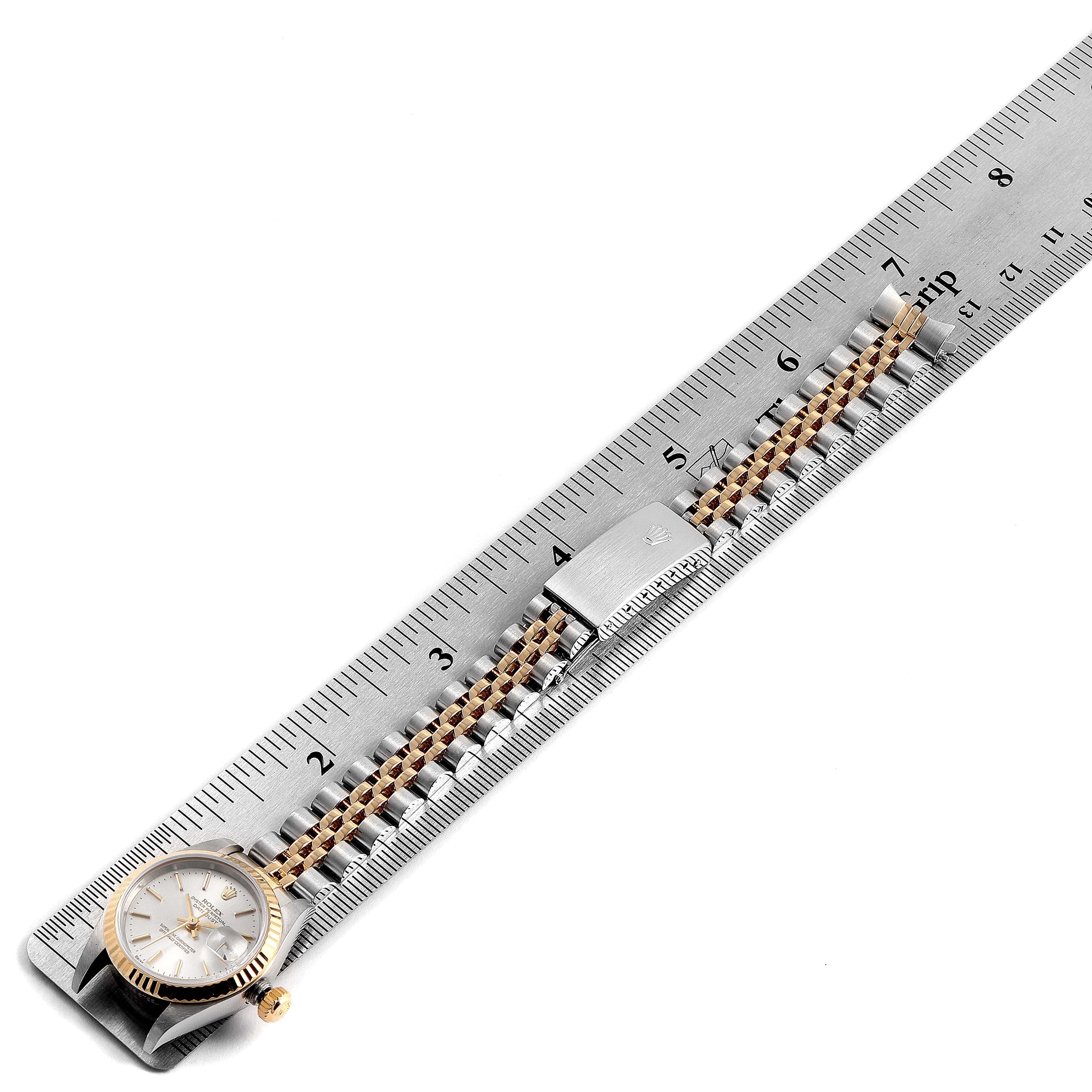 The Rolex Datejust 79173 Women's Steel and Gold (two tone) Silver Dial 79173 Women's Steel and Gold (two tone) Silver Dial watch is shown laid out with its band fully extended alongside a metal ruler.