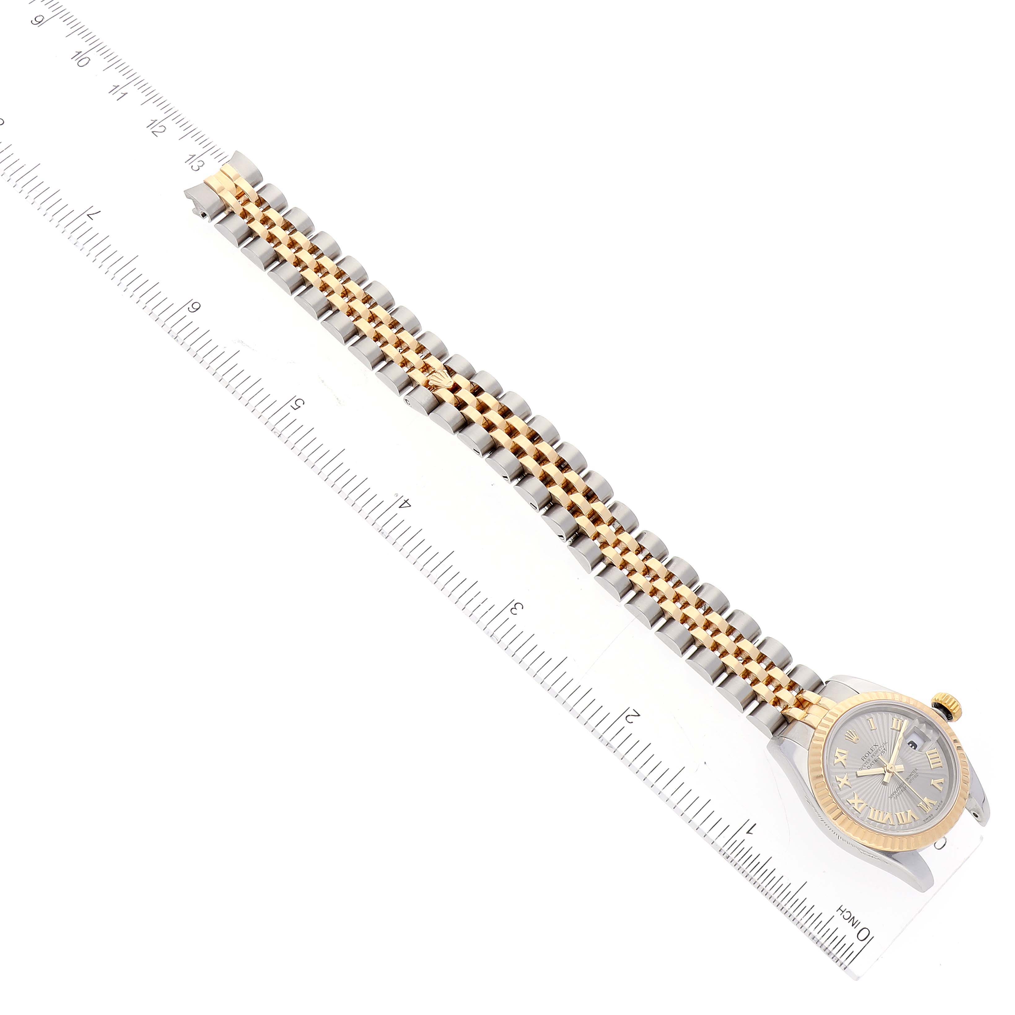 The image shows a Rolex Datejust 179173 Women's Steel and Gold (two tone) Silver Dial 179173 Women's Steel and Gold (two tone) Silver Dial watch aligned with a ruler, displaying the dial and two-tone bracelet from an aerial perspective.