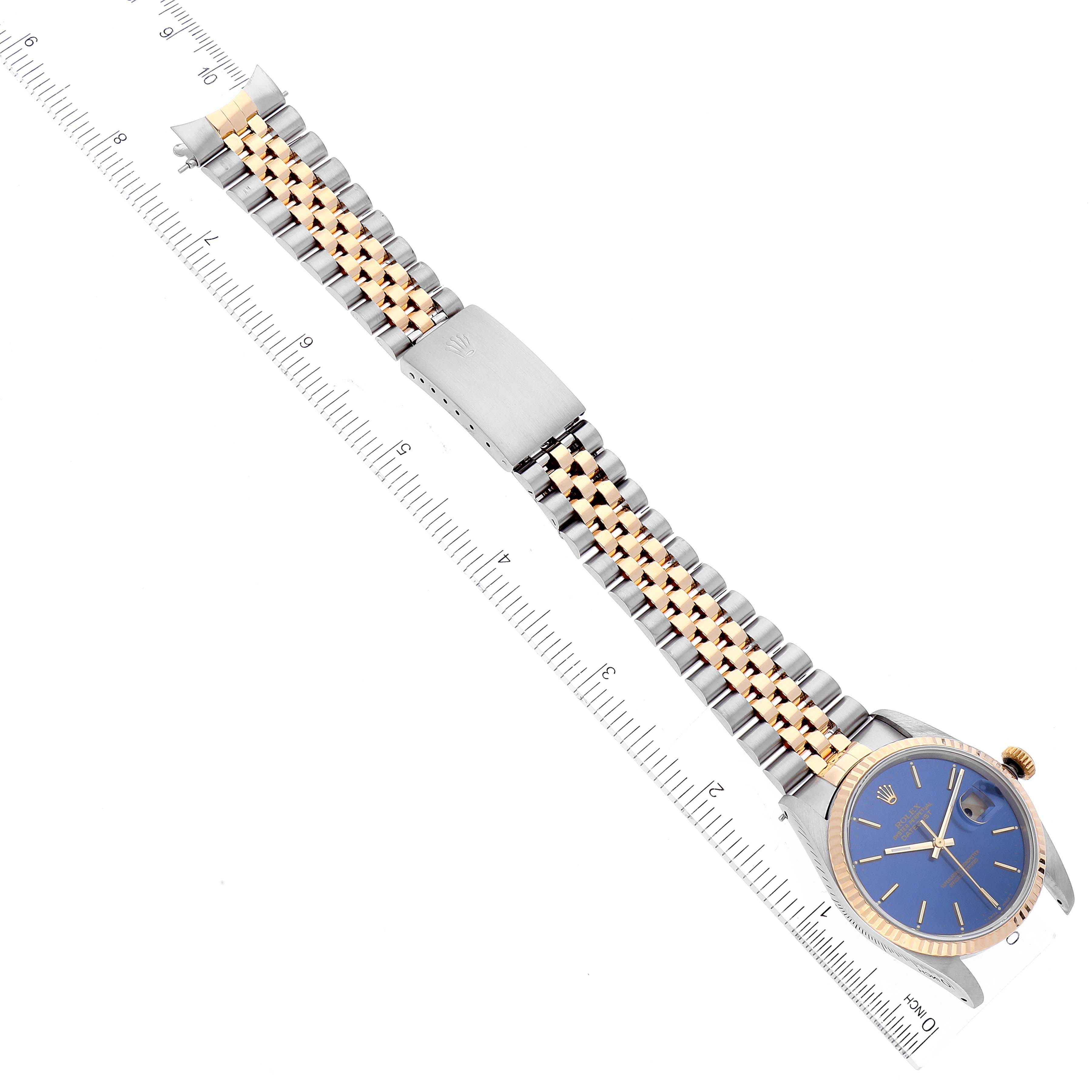 The Rolex Datejust 16233 Men's Steel and Gold (two tone) Blue Dial 16233 Men's Steel and Gold (two tone) Blue Dial watch is shown from a top-down angle, revealing its bracelet, face, and clasp alongside a measurement ruler.