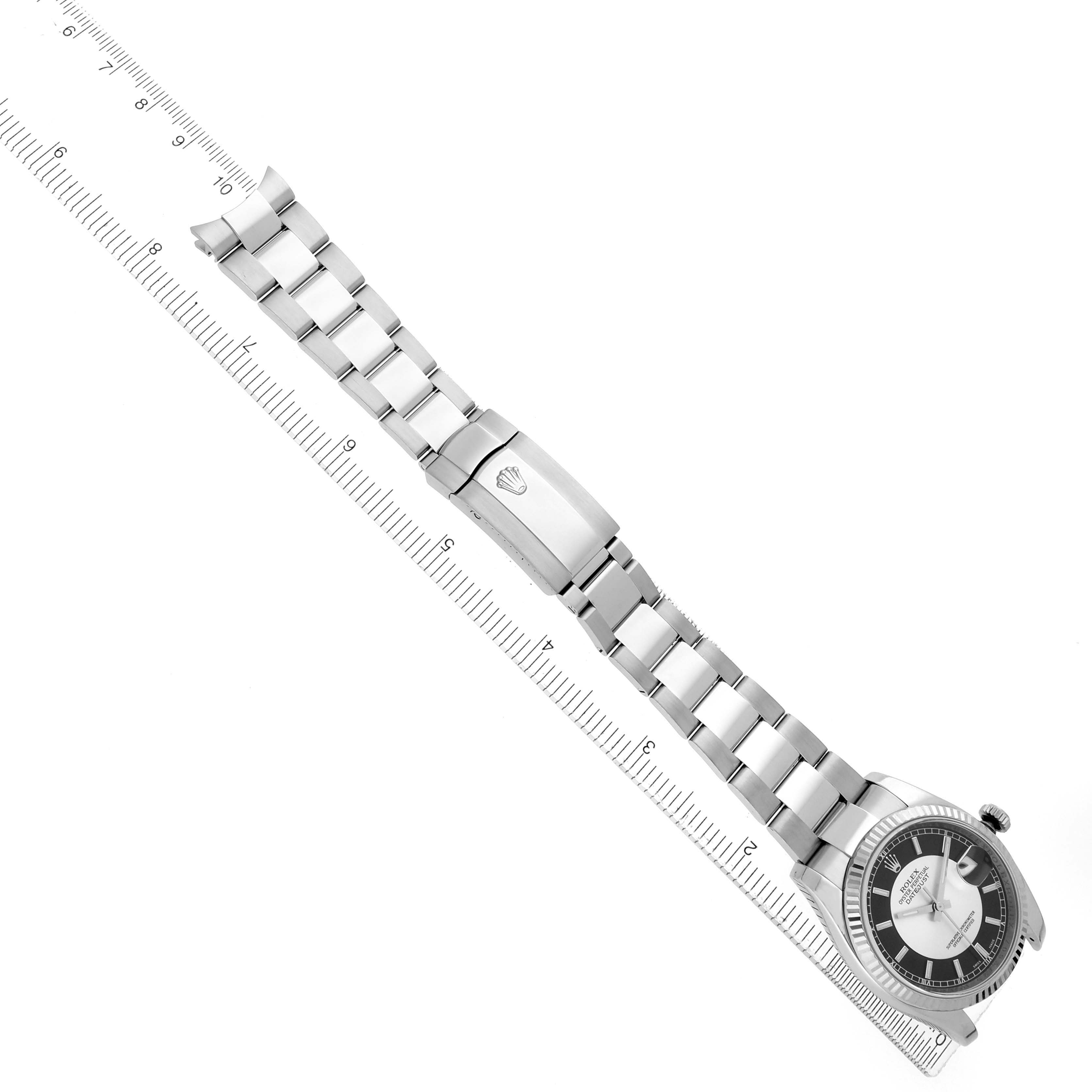 The image shows a Rolex Datejust 116234 Men
s Stainless Steel Black Dial watch at an angle, displaying the full bracelet, clasp, and face alongside a measuring ruler.