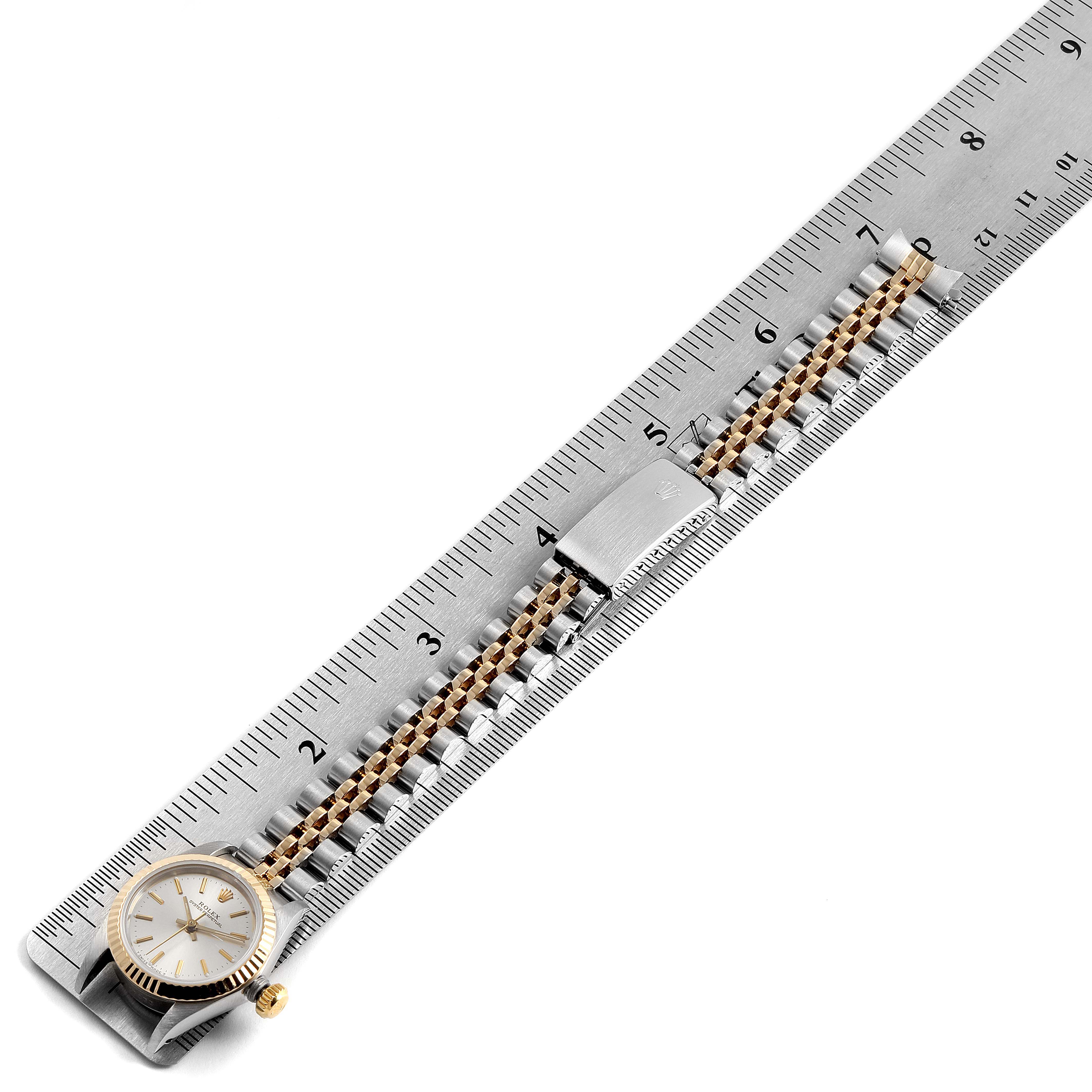 This image shows a Rolex Oyster Perpetual 67193 Women
s Steel and Gold (two tone) Silver Dial 67193 Women
s Steel and Gold (two tone) Silver Dial watch with its band and clasp laid alongside a ruler for measurement.