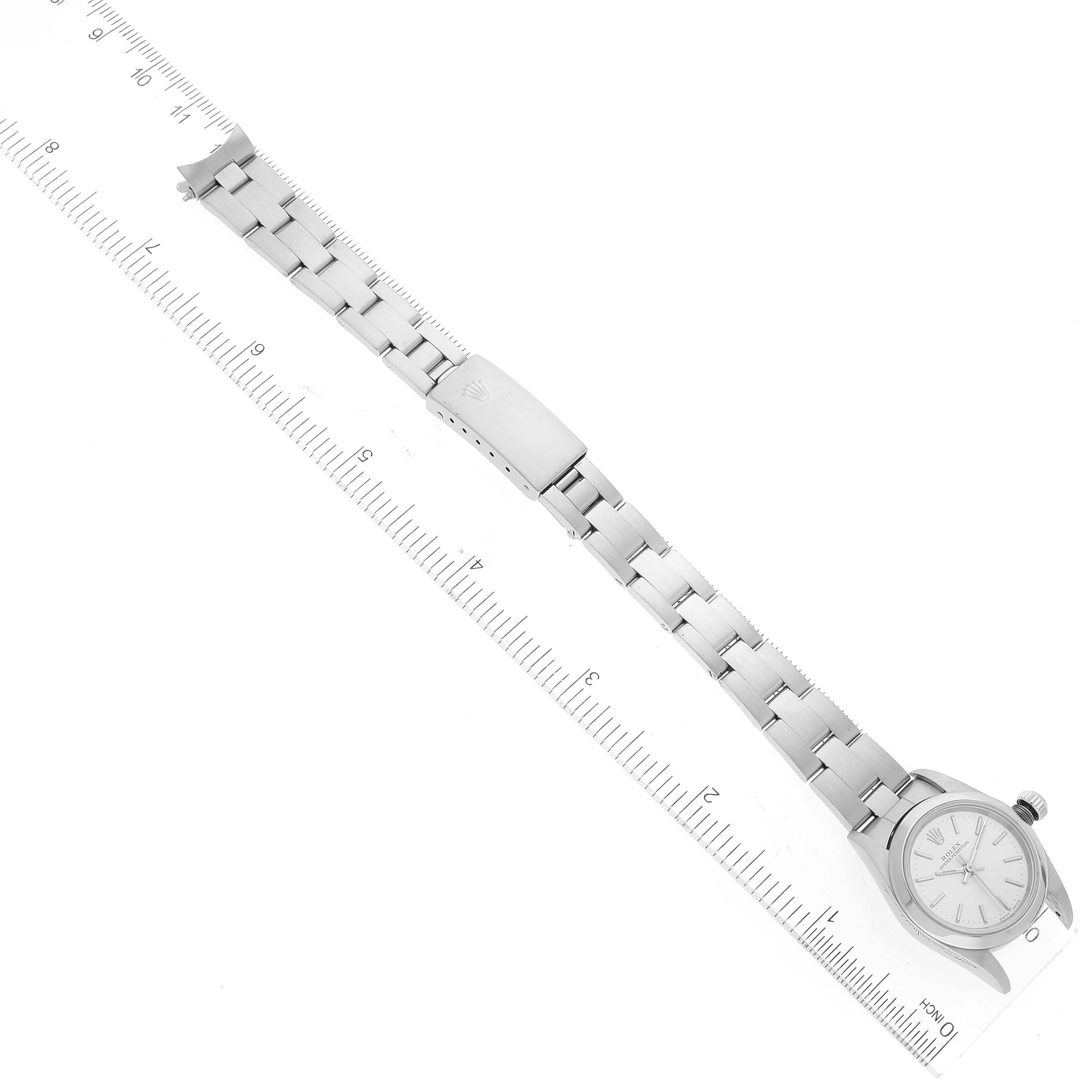 The Rolex Oyster Perpetual 76080 Women's Stainless Steel Silver Dial 76080 Women's Stainless Steel Silver Dial watch is shown from a top-down view, featuring the full bracelet and clasp, along with a ruler for scale.