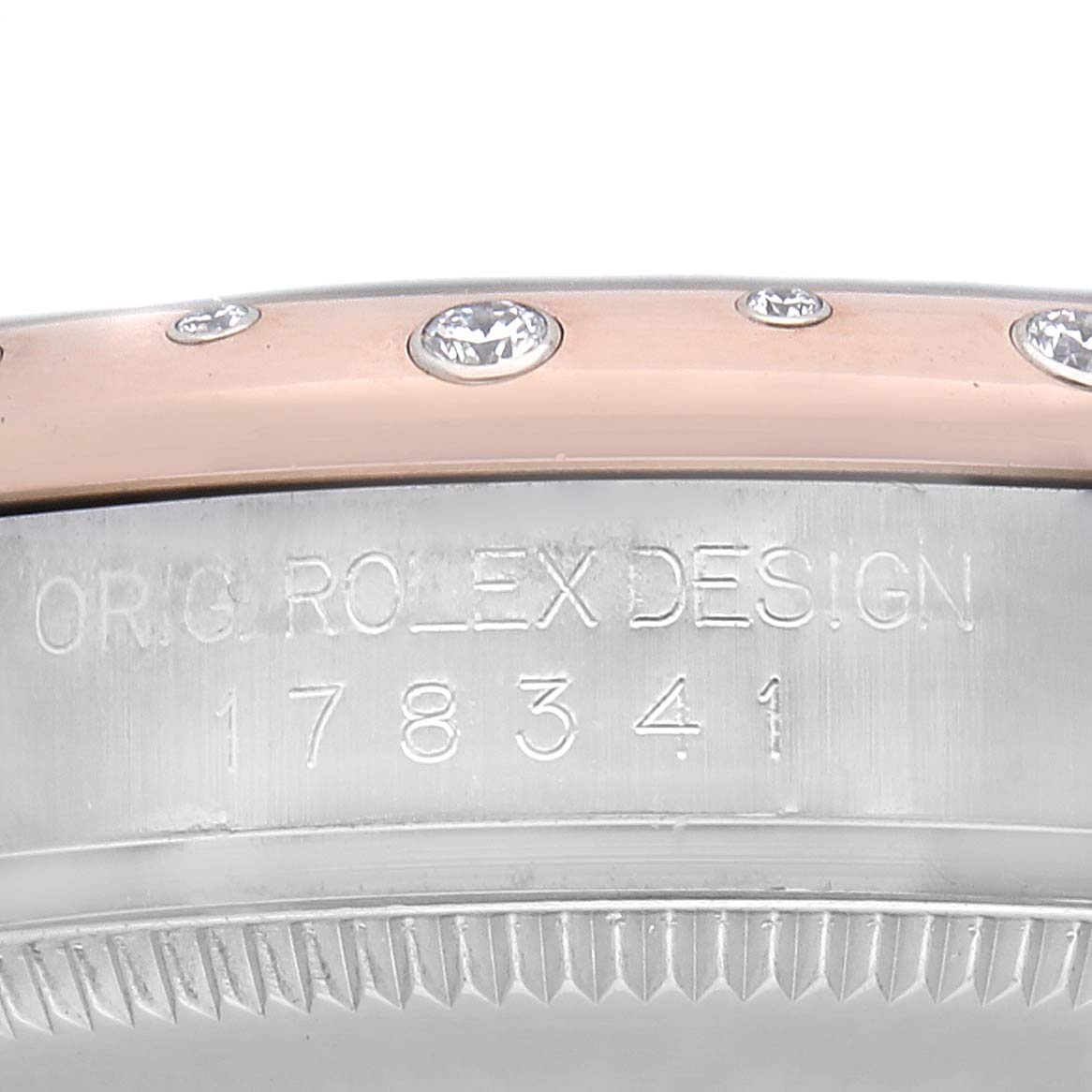 The image shows a side view of a Mid-Size Rolex watch
s bezel with diamond accents and engraving details on the case.