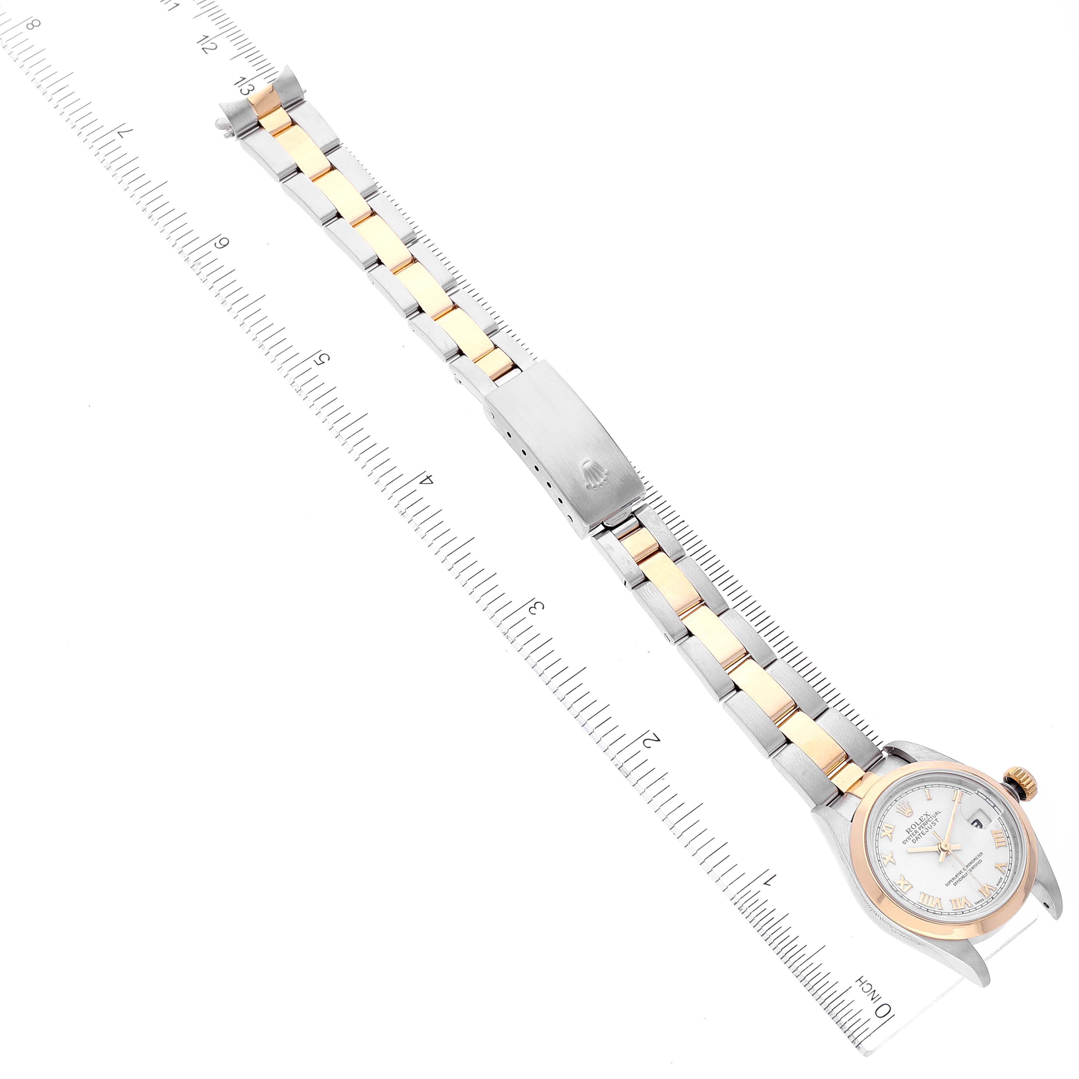 The image shows an overhead view of a Rolex Datejust 79163 Women's Steel and Gold (two tone) White Dial 79163 Women's Steel and Gold (two tone) White Dial watch, displaying its face, bracelet, and clasp along with a measuring ruler.