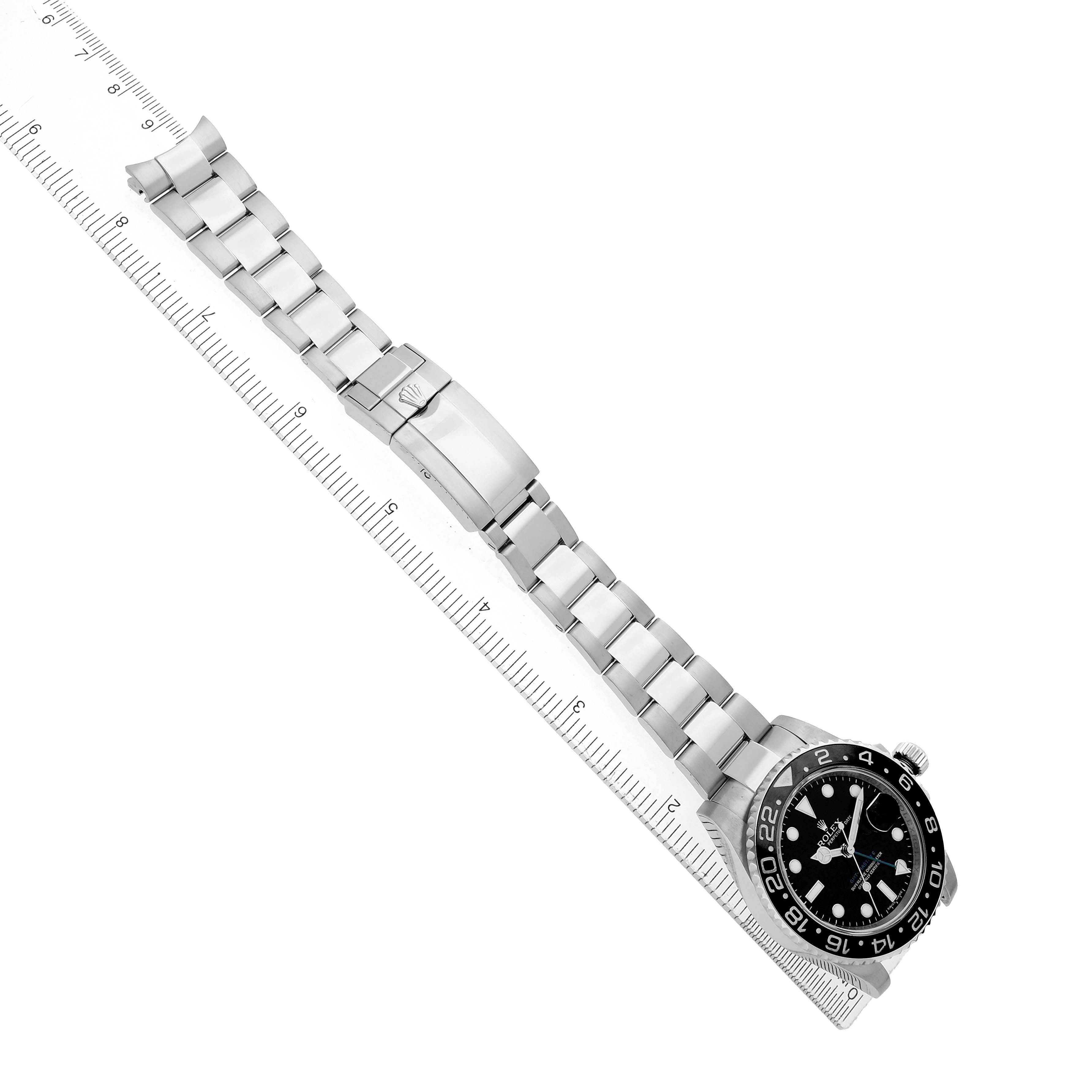 The image shows a Rolex GMT-Master 116710 Men
s Stainless Steel Black Dial watch laid flat with its face, clasp, and metal bracelet aligned along a ruler.