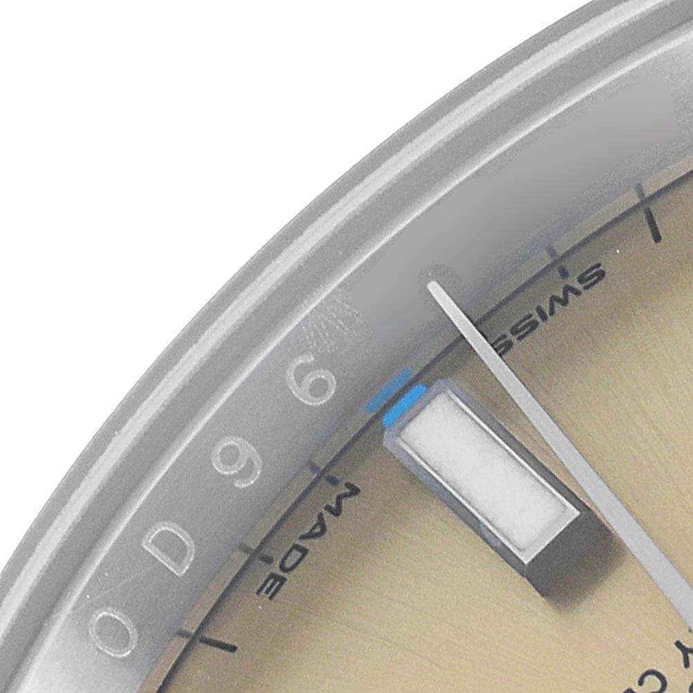 This close-up image of the Rolex Oyster Perpetual 114200 Men's Stainless Steel Champagne Dial 114200 Men's Stainless Steel Champagne Dial watch shows part of the dial, a luminous marker, and the "Swiss" text.