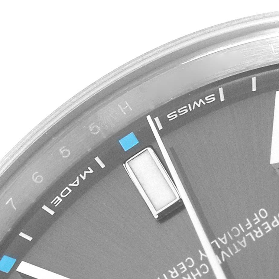 The image shows a close-up of the Rolex Oyster Perpetual 114300 Men's Stainless Steel Grey Dial watch face, displaying hour markers, part of the dial, and text.
