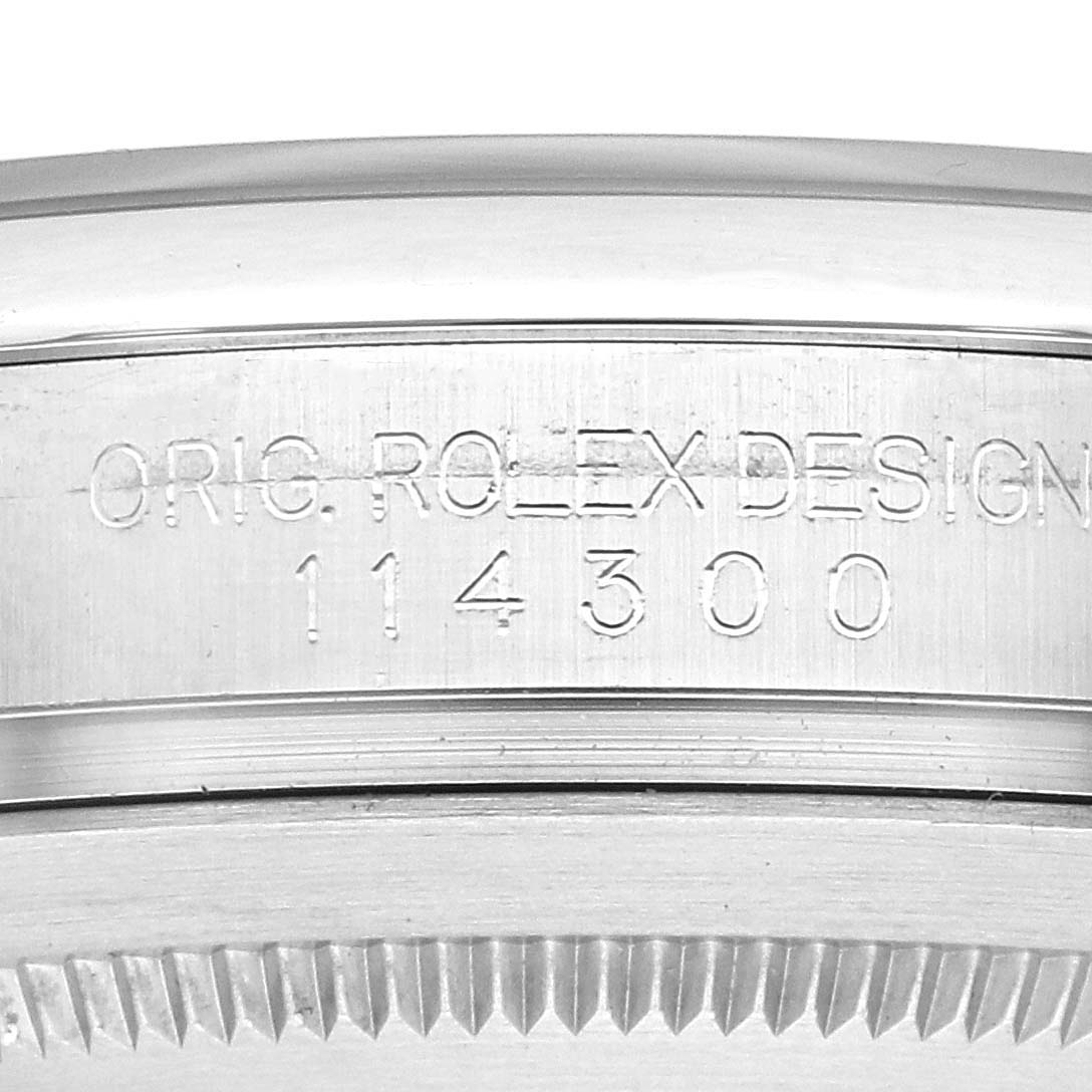 The image shows the side engraving on the case of a Rolex Oyster Perpetual 114300 Men's Stainless Steel Grey Dial, displaying "ORIG. ROLEX DESIGN" and model number 114300.