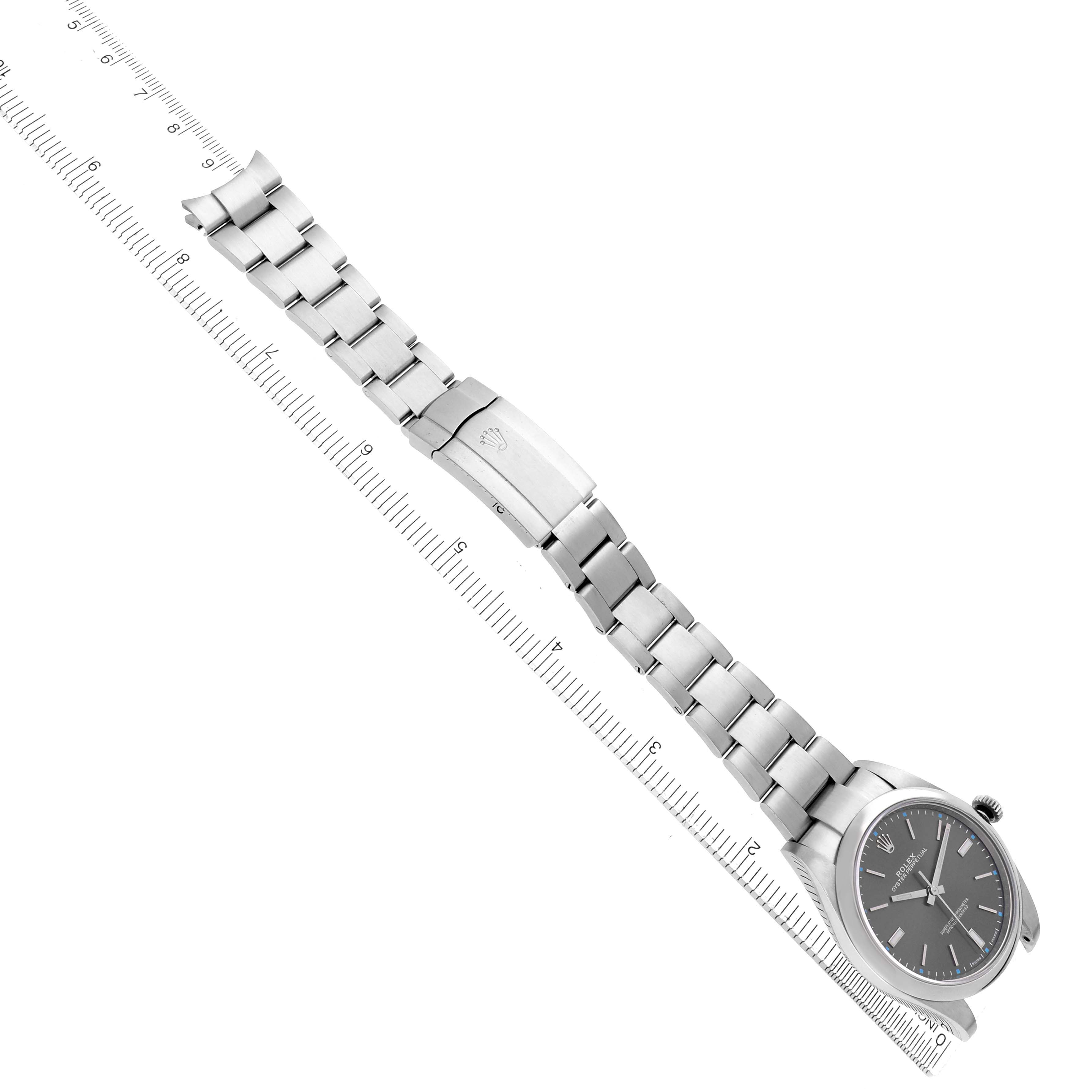 The Rolex Oyster Perpetual 114300 Men's Stainless Steel Grey Dial watch is displayed diagonally, showcasing its bracelet, clasp, and face alongside a ruler for scale.