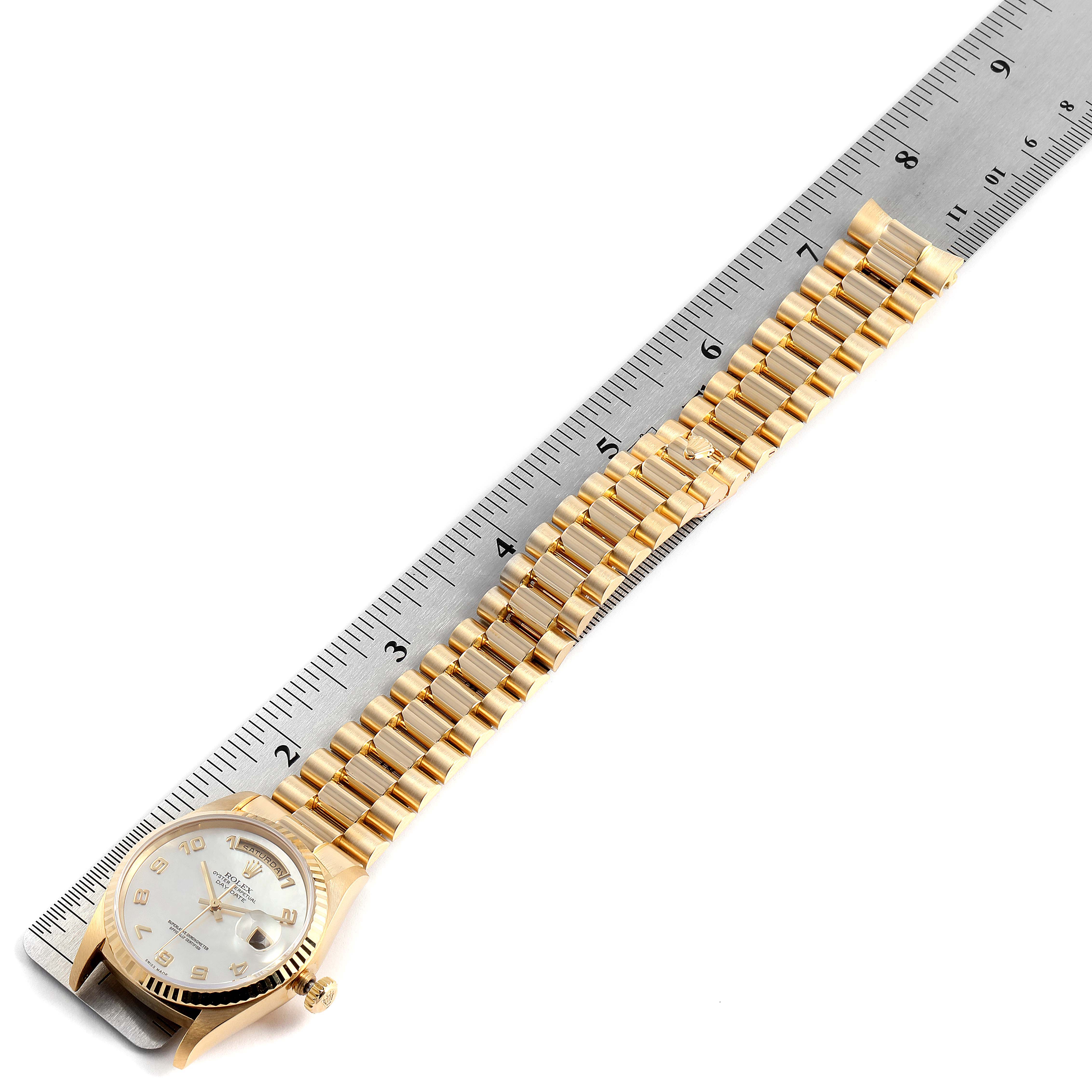 The Rolex President 18238 Men's Yellow Gold Mother of Pearl Dial 18238 Men's Yellow Gold Mother of Pearl Dial model watch is shown from a top angle alongside a ruler, displaying its face and bracelet.