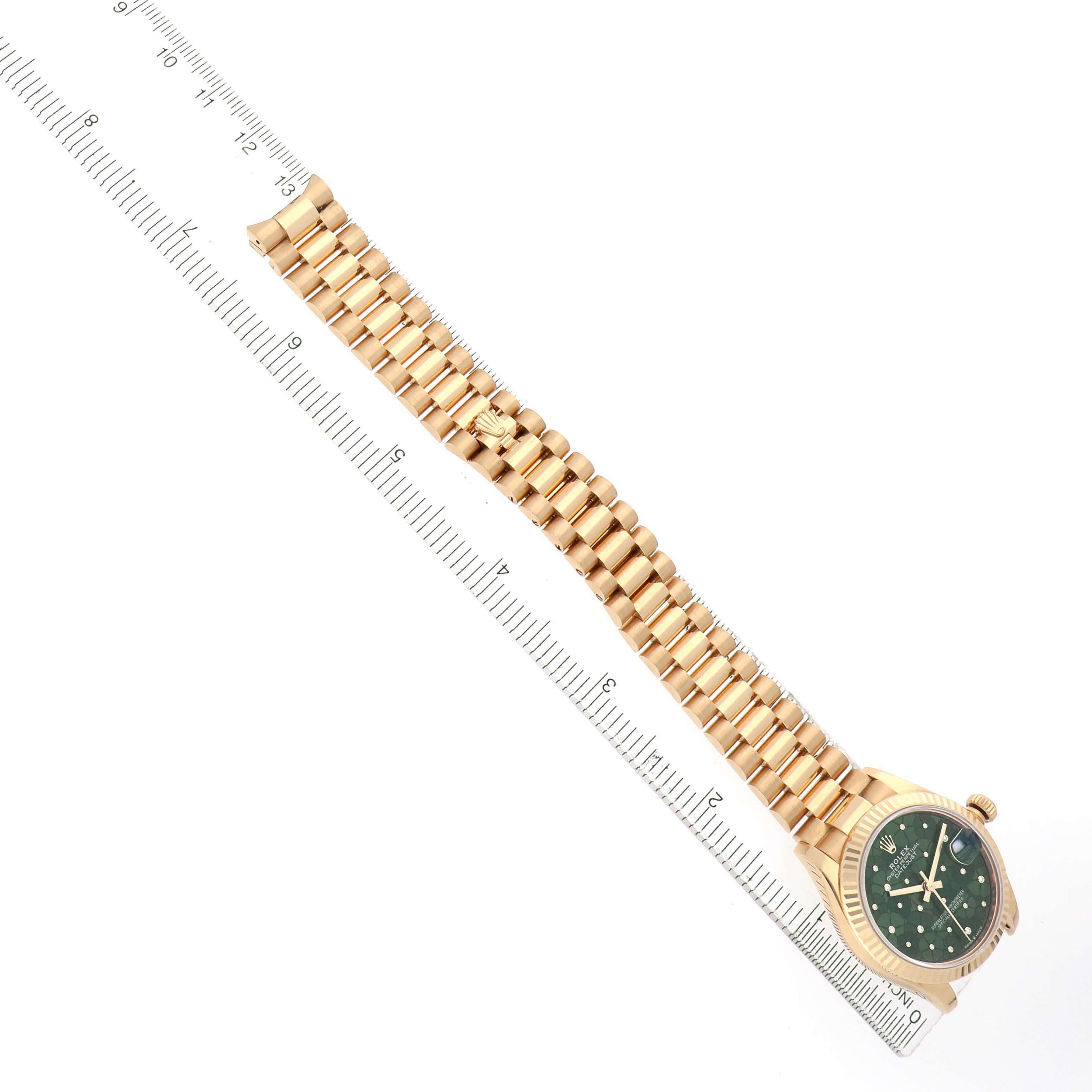 The Rolex President 278278 Women
s Yellow Gold Green Dial watch is shown from a top view, displaying the band, face, and part of the clasp, next to a ruler.