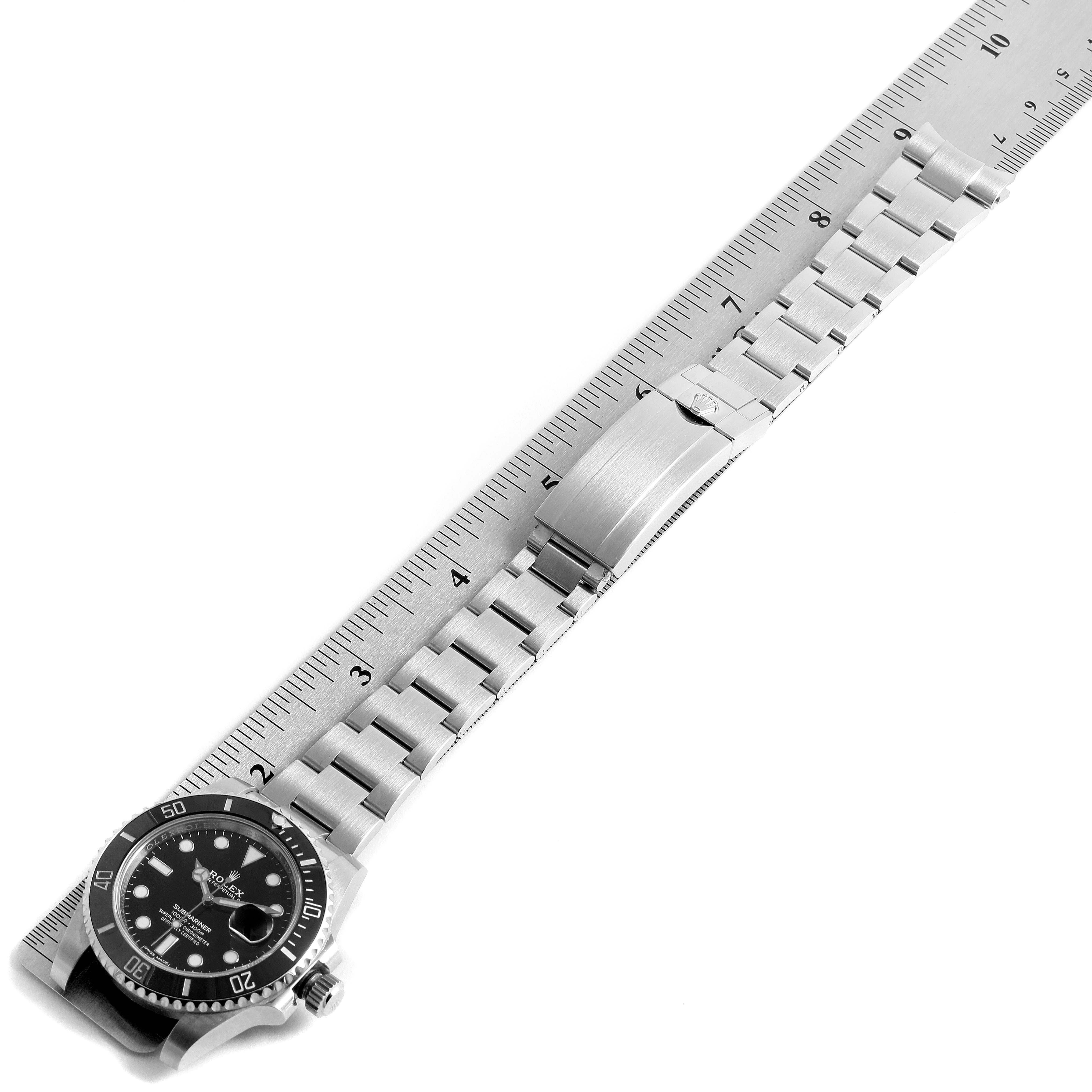 The Rolex Submariner 116610 Men's Stainless Steel Black Dial 116610 Men's Stainless Steel Black Dial watch is displayed showing the face, bezel, and full metal bracelet laid alongside a ruler.