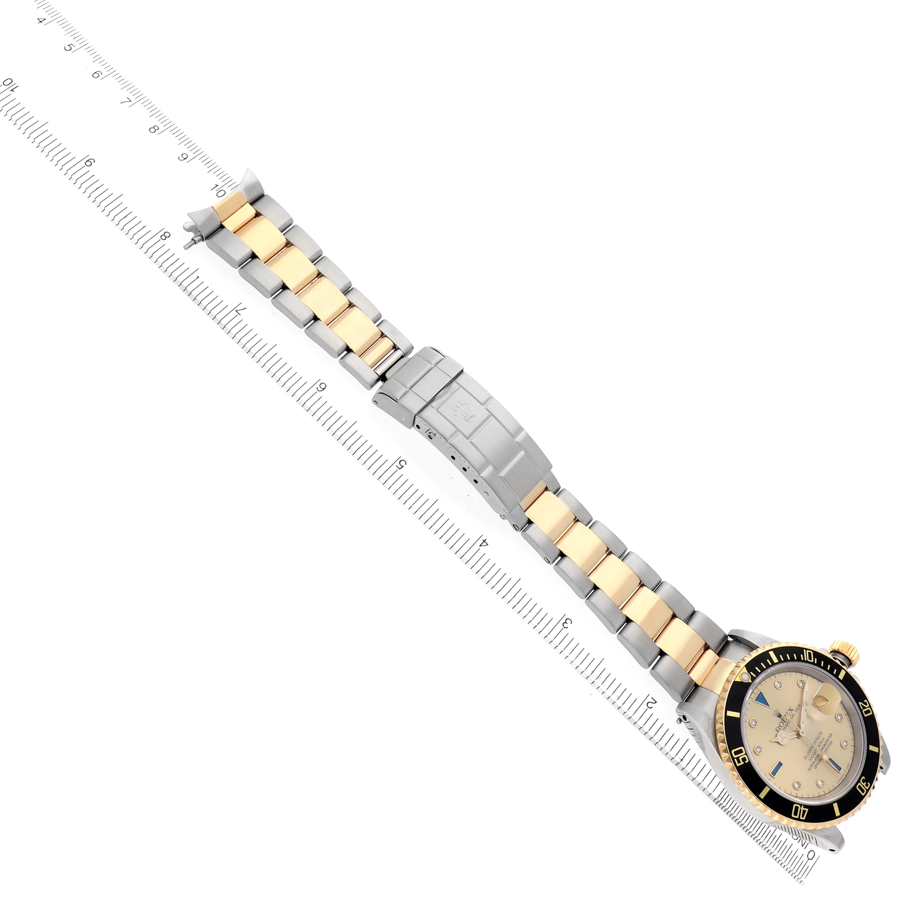 The Rolex Submariner 16613 Men
s Steel and Gold (two tone) Champagne Dial is shown at an angle displaying its face, bezel, and two-tone bracelet along a ruler for scale.