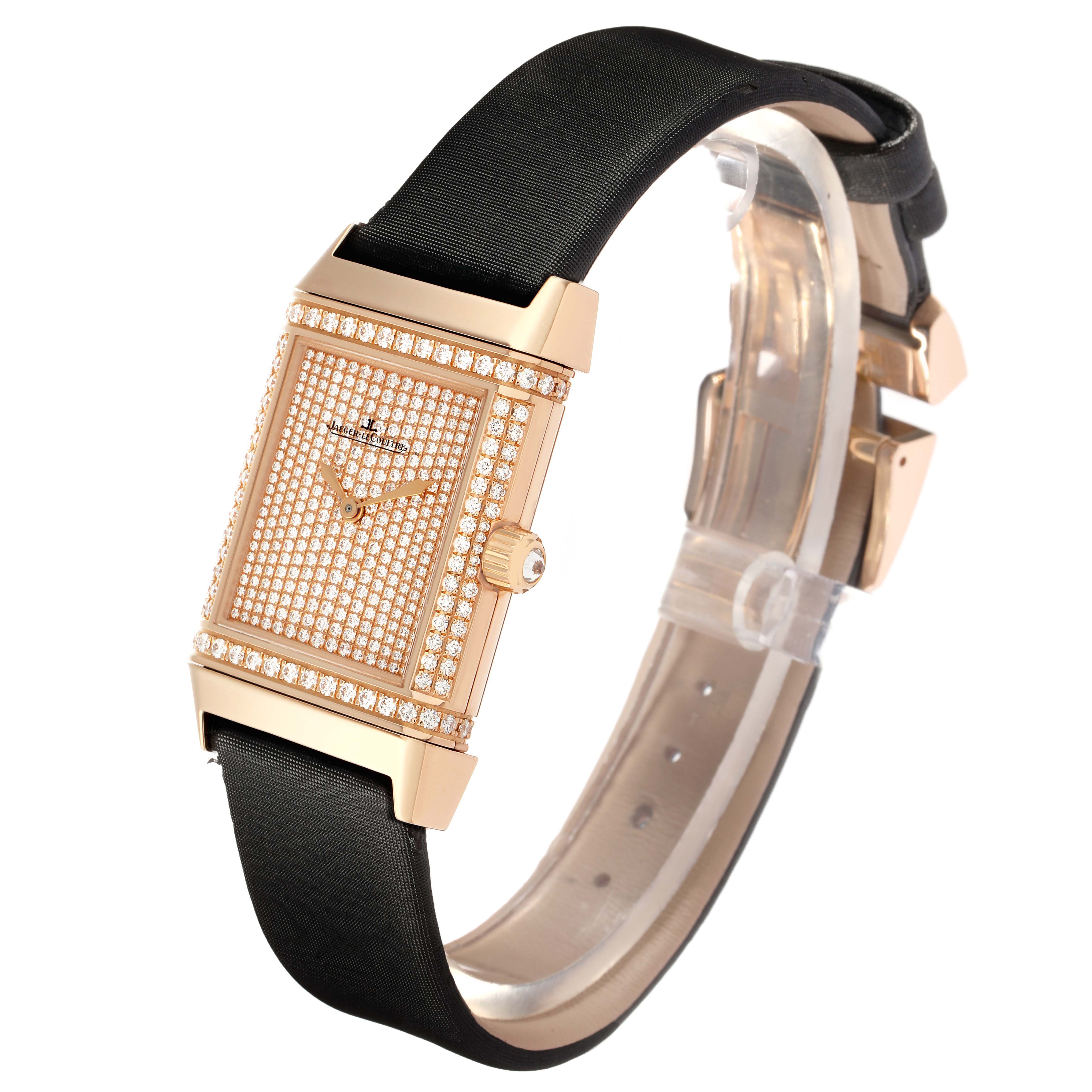 The Jaeger LeCoultre Reverso Q2562407 Women's Rose Gold Pink Dial watch is shown at a three-quarter angle, highlighting its diamond-studded face and black strap.