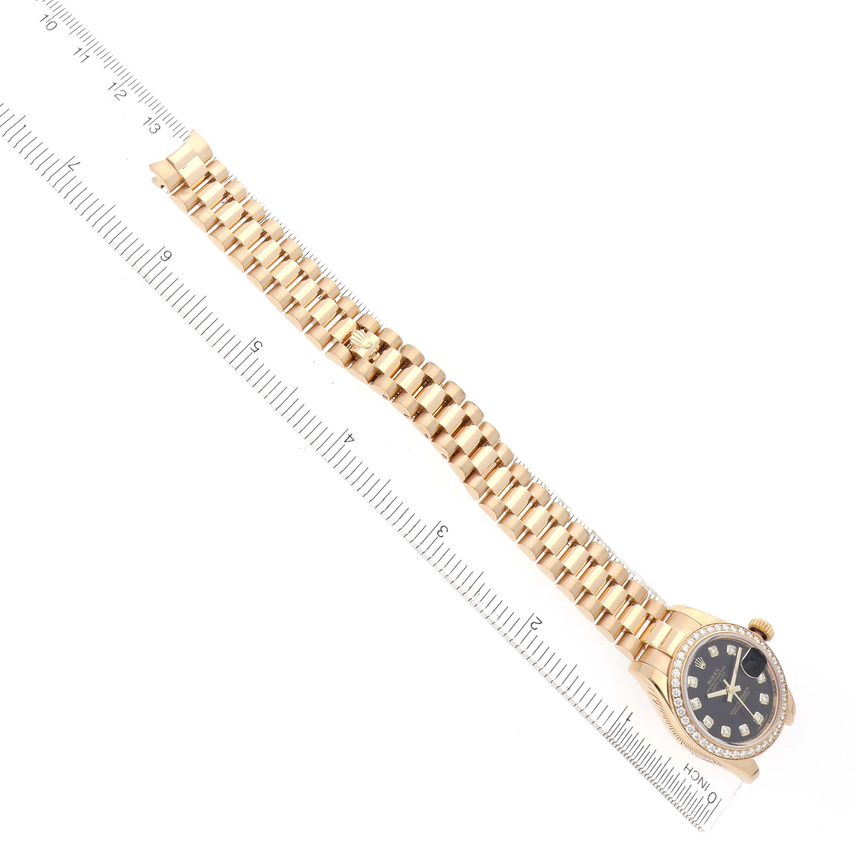 The Rolex Datejust 179138 Women
s Yellow Gold Black Dial watch is shown at an angle displaying its face, bracelet, and a ruler for scale.