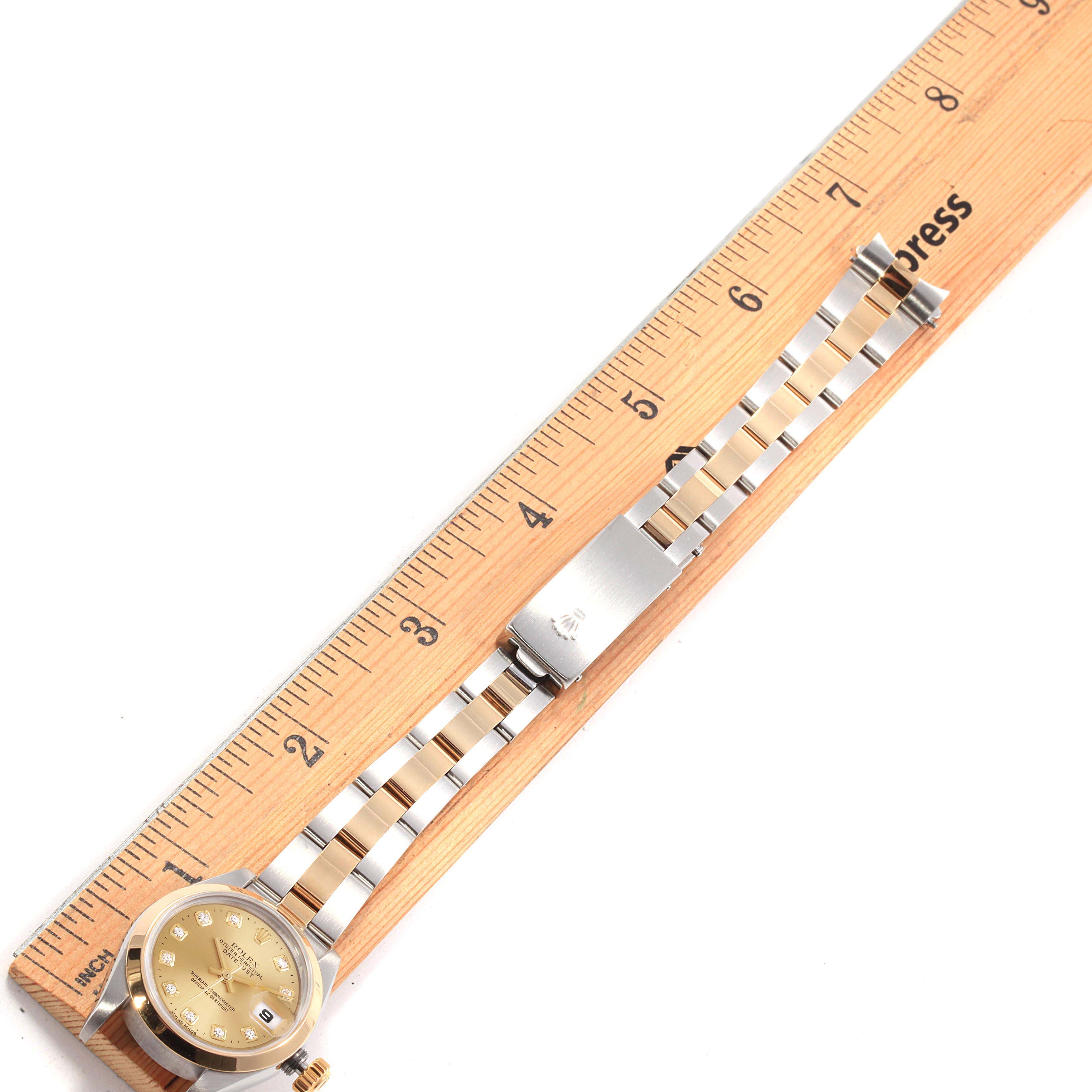 The Rolex Datejust 79163 Women's Steel and Gold (two tone) Champagne Dial 79163 Women's Steel and Gold (two tone) Champagne Dial watch is displayed flat with the face and strap extended along a wooden ruler, showcasing measurement details.