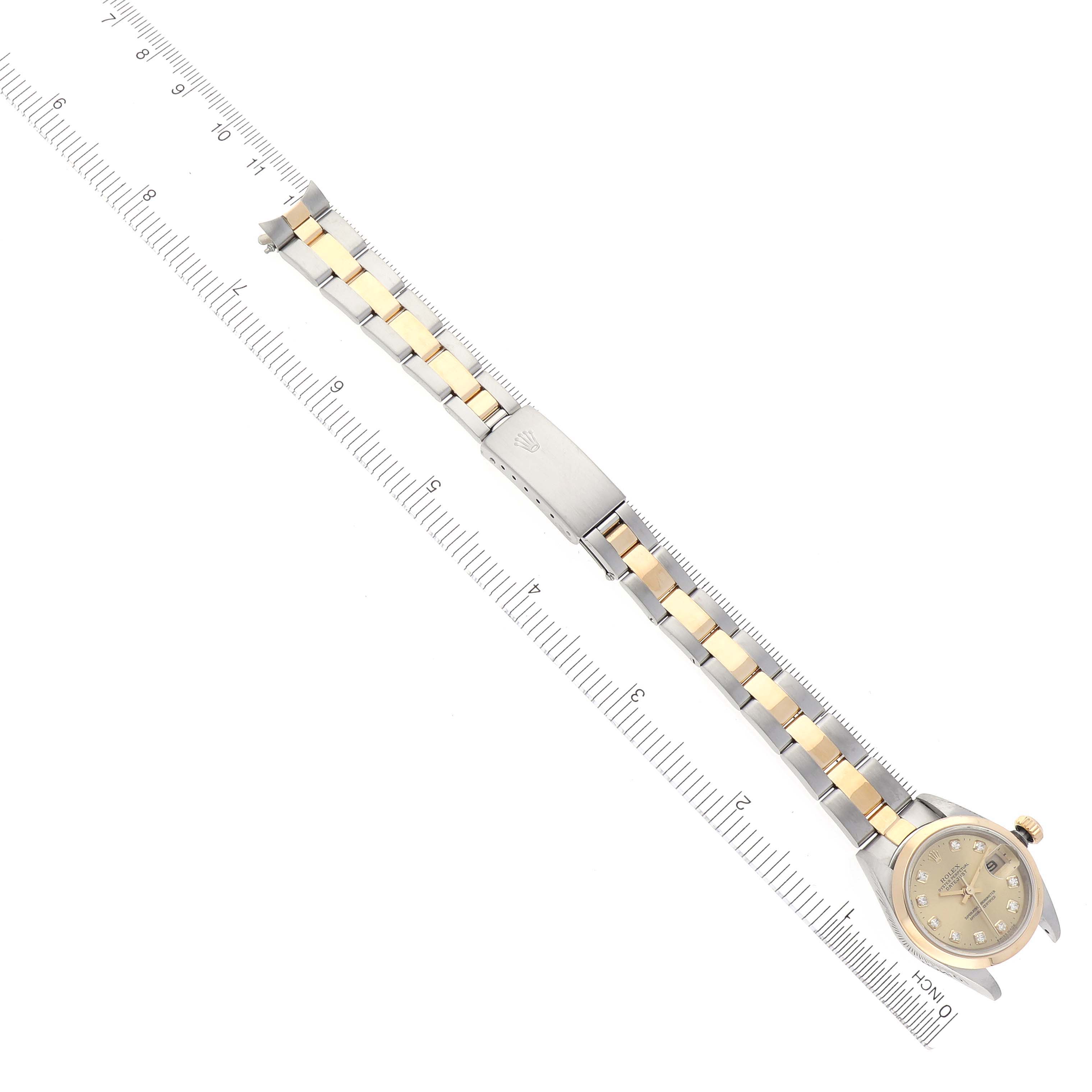The image shows a Rolex Datejust 79163 Women
s Steel and Gold (two tone) Champagne Dial 79163 Women
s Steel and Gold (two tone) Champagne Dial watch laid flat with its bracelet extended along a ruler, displaying the face, bracelet, and clasp.