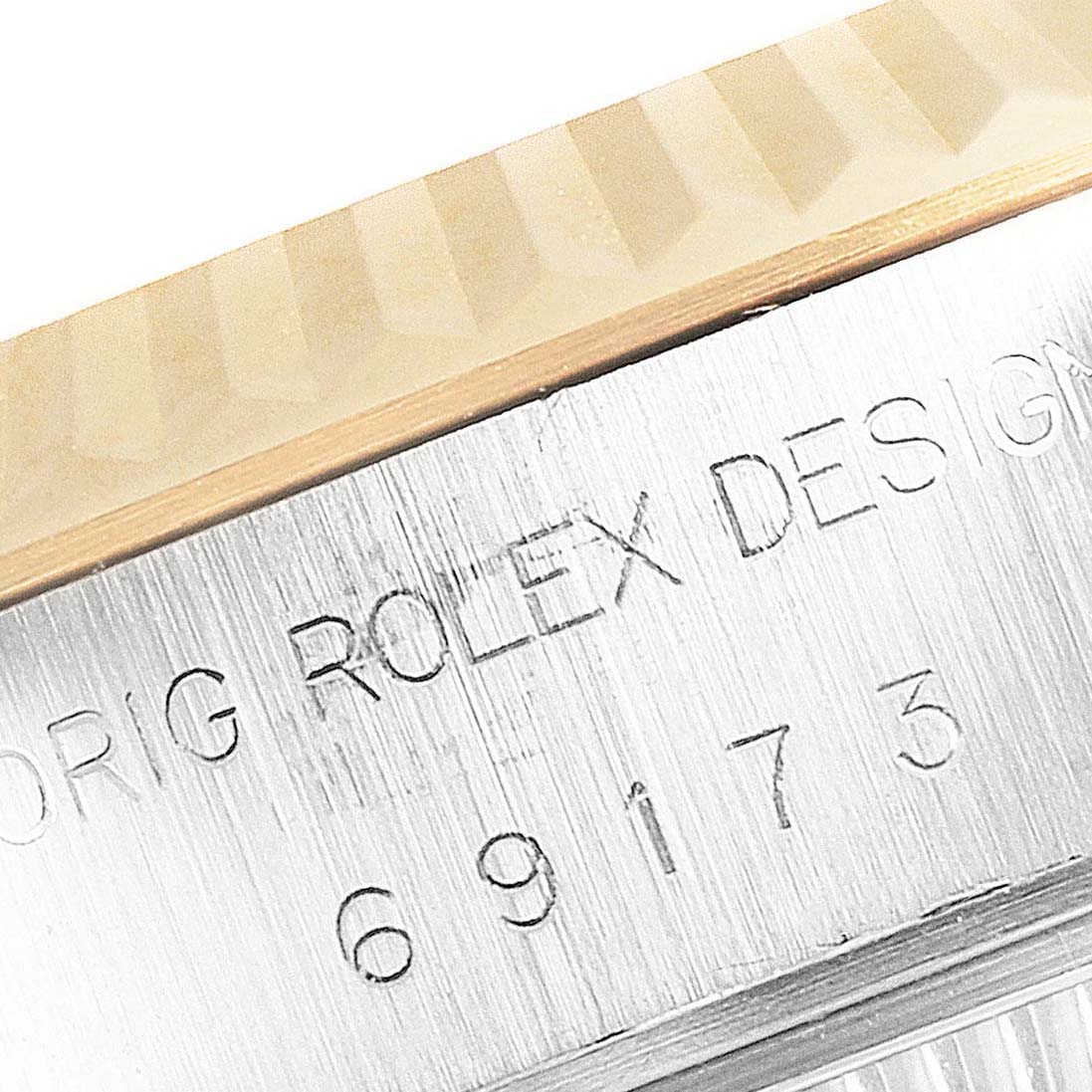 The image shows a close-up of the Rolex Datejust 69173 Women's Steel and Gold (two tone) Champagne Dial 69173 Women's Steel and Gold (two tone) Champagne Dial model's bezel and case with engraved design and serial numbers.