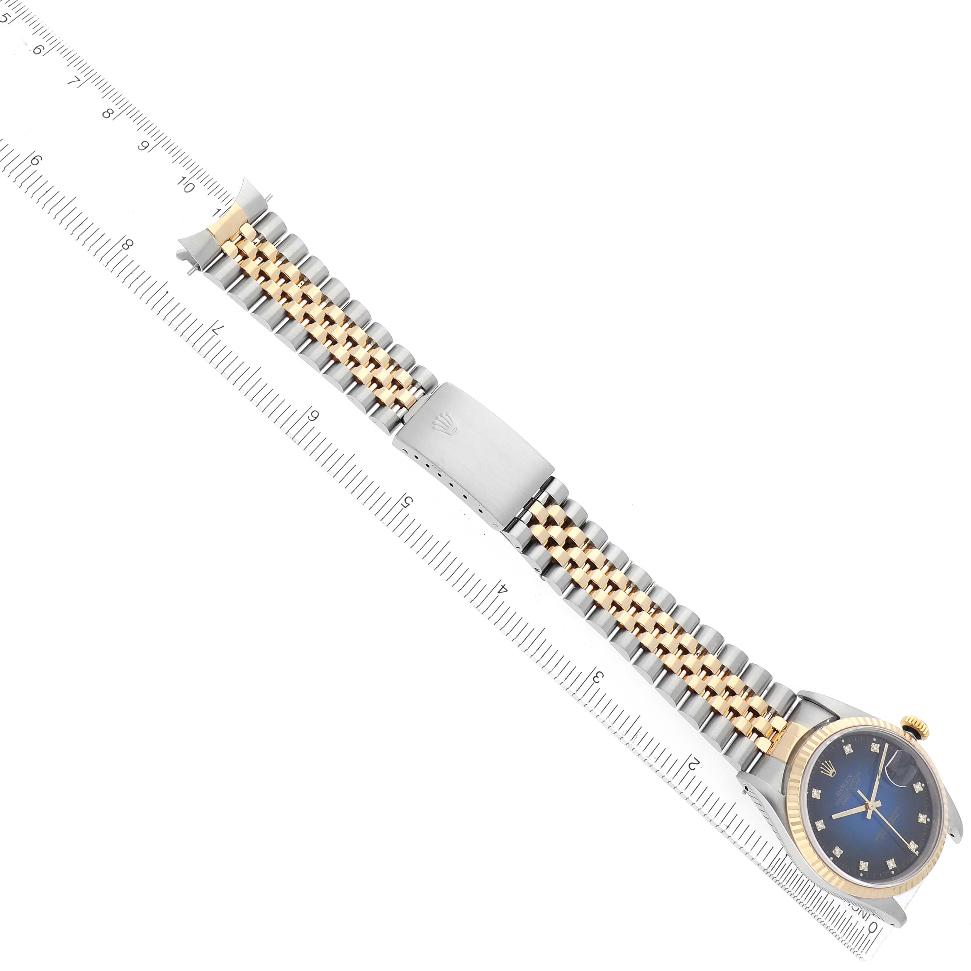 The Rolex Datejust 16233 Men
s Steel and Gold (two tone) Blue Dial watch is shown from a top view, displaying the full face, bracelet, and clasp alongside a measuring ruler.