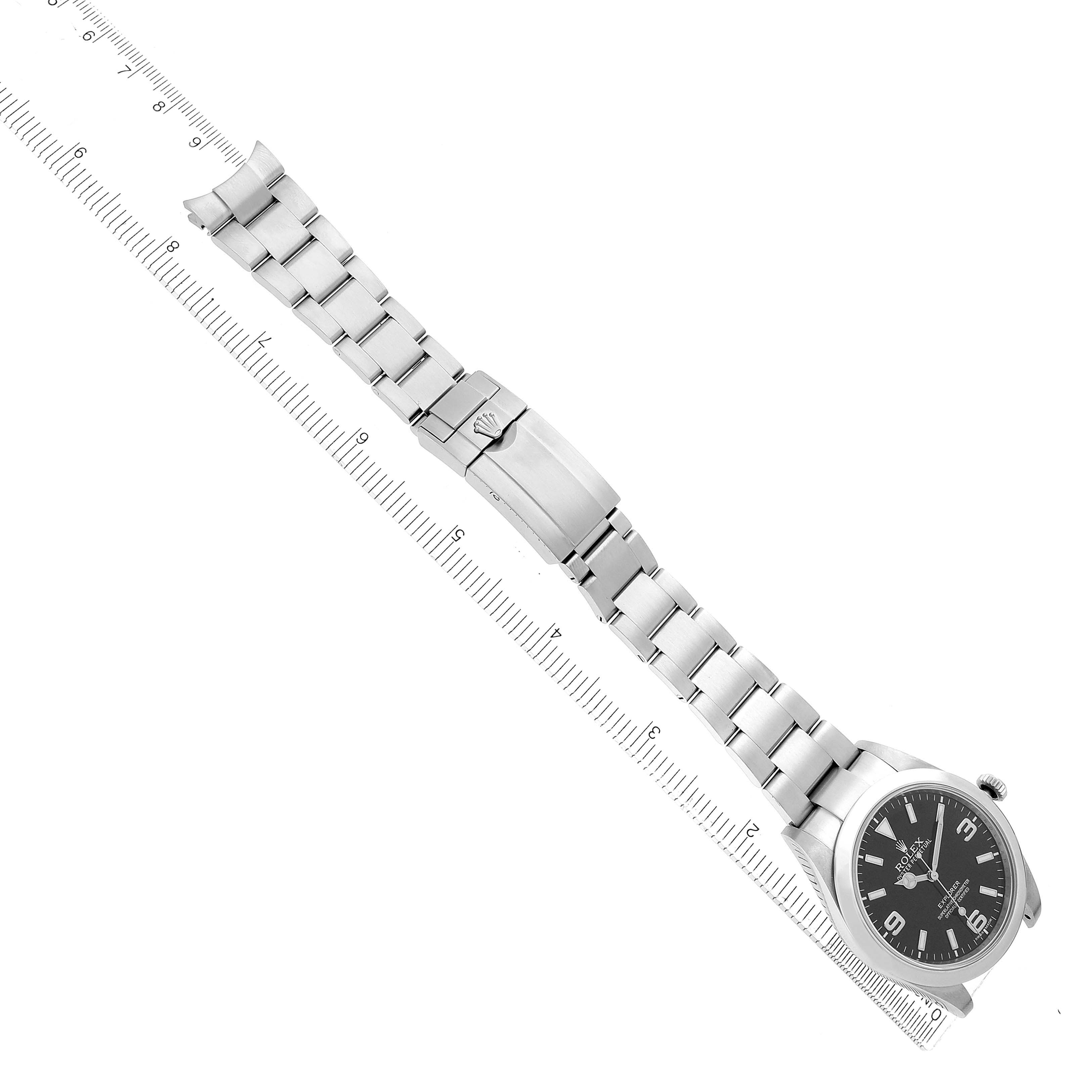 The Rolex Explorer 214270 Men
s Stainless Steel Black Dial watch is shown at an oblique angle, displaying the face and metal bracelet with clasp, alongside a ruler for scale.