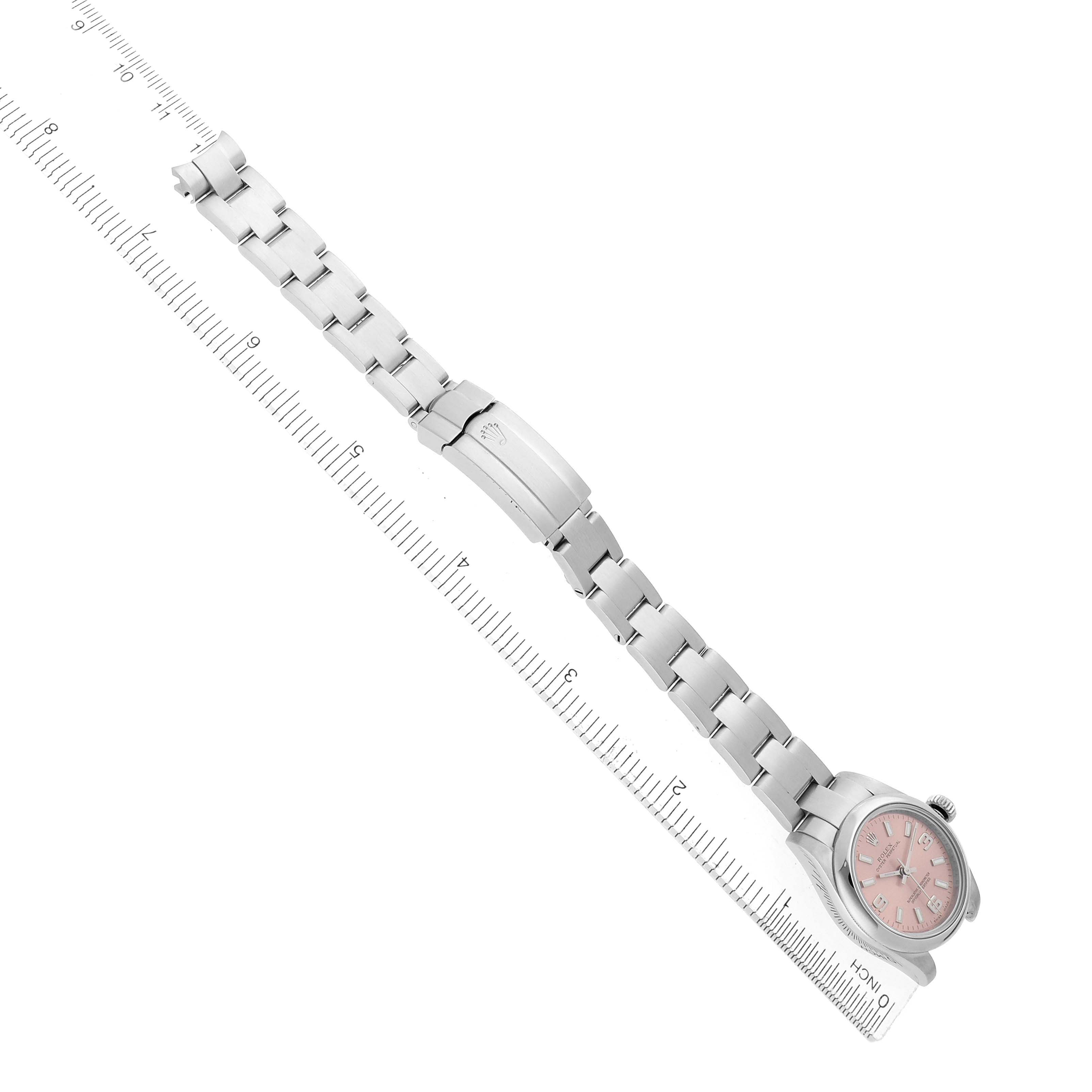 The Rolex Oyster Perpetual 176200 Women
s Stainless Steel Pink Dial watch is shown from a top angle, highlighting the bracelet, clasp, and pink dial aligned with a ruler.