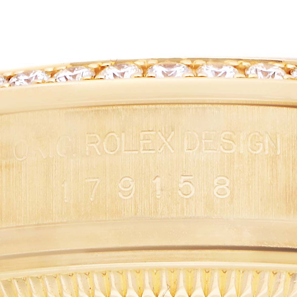 The image shows a close-up of the Rolex President 179158 Women
s Yellow Gold Silver Dial watch
s bezel and part of the engraved side, featuring diamonds.