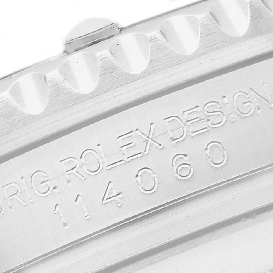 The image shows a close-up of the engraved side of a Rolex Submariner 114060 Men
s Stainless Steel Black Dial, featuring part of the bezel and reference number.