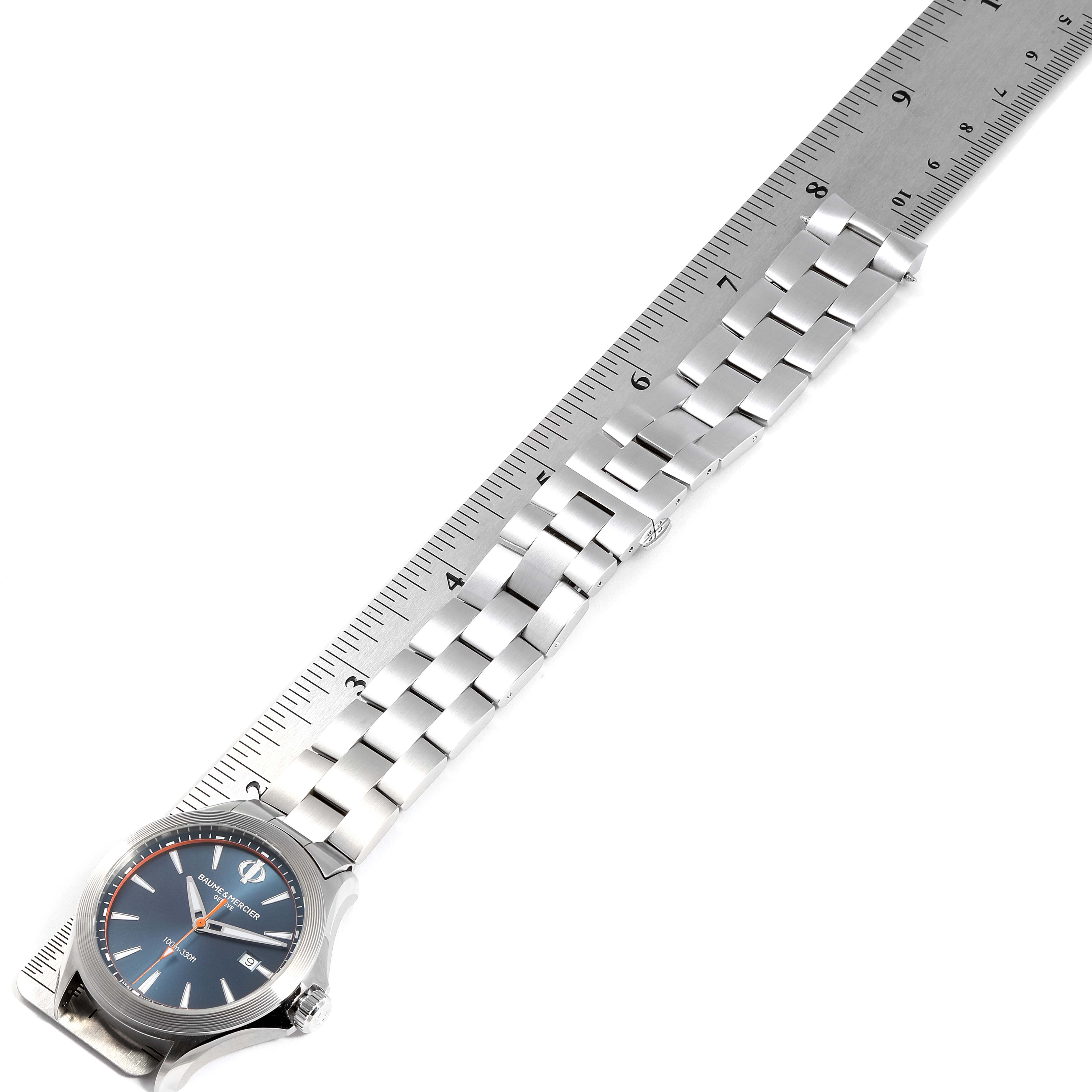 The image shows a Baume & Mercier Clifton M0A10413 Men's Stainless Steel Blue Dial M0A10413 Men's Stainless Steel Blue Dial model watch, angled diagonally with its face and metal bracelet alongside a ruler.