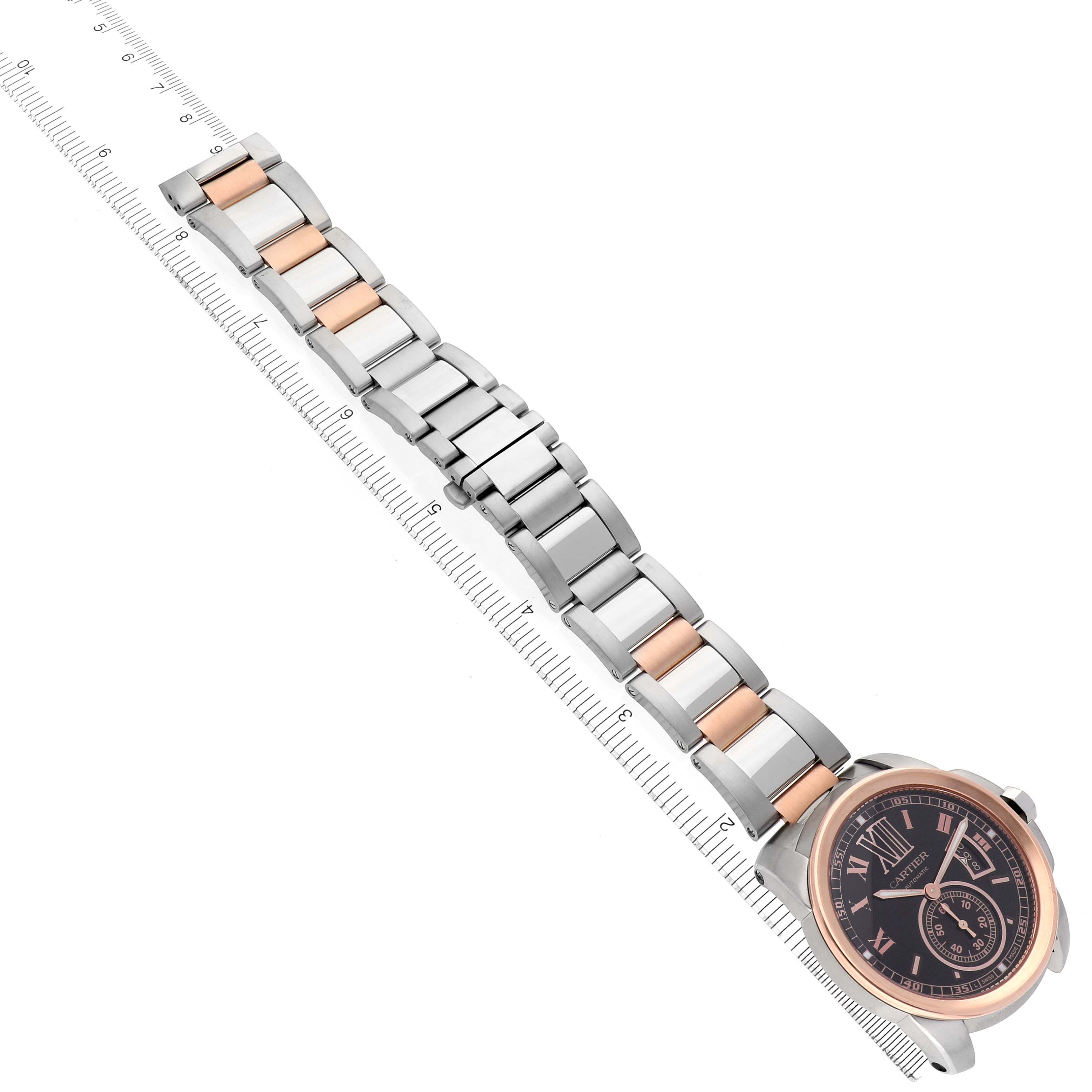 The image shows the entire Calibre de Cartier watch by Cartier, displayed flat with its bracelet extended alongside a ruler for measurement.