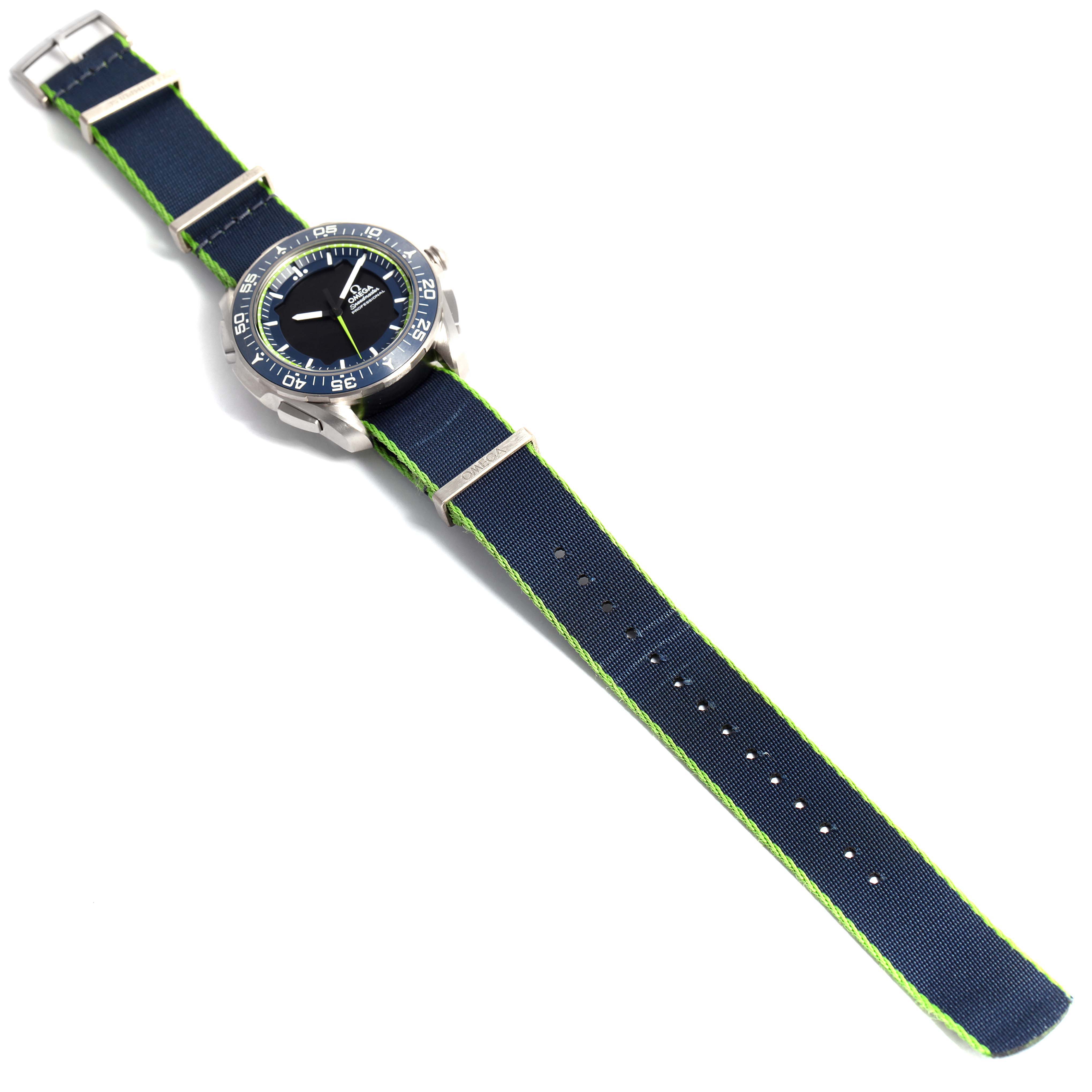 The image shows an Omega Speedmaster 318.92.45.79.03.001 Men's Platinum Blue Dial 318.92.45.79.03.001 Men's Platinum Blue Dial watch at a top-down angle, displaying the face, case, and full navy and green strap.