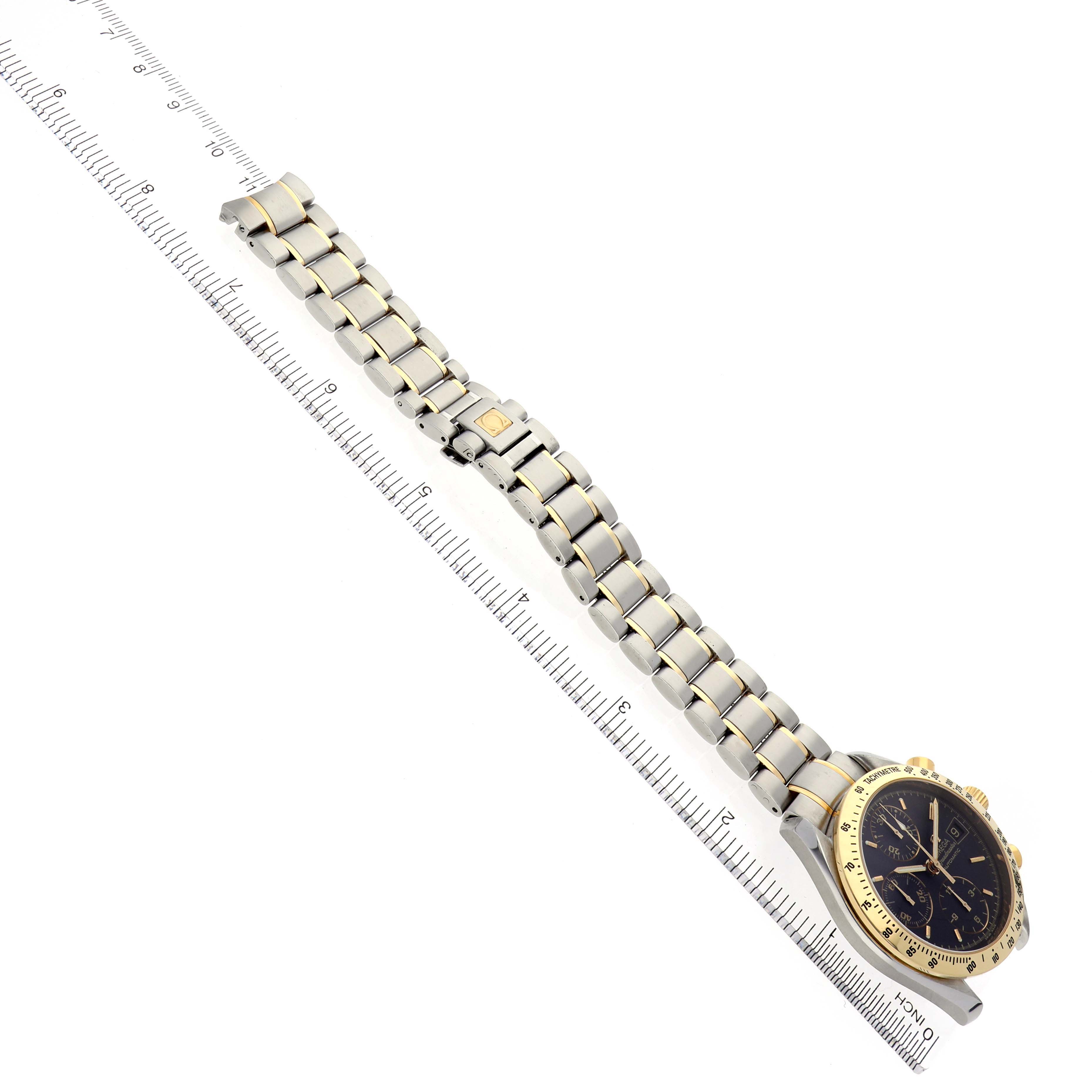 This image shows an Omega Speedmaster 3313.50.00 Men's Steel and Gold (two tone) Black Dial 3313.50.00 Men's Steel and Gold (two tone) Black Dial watch with a bracelet at a slight side angle, placed adjacent to a ruler for measurement.