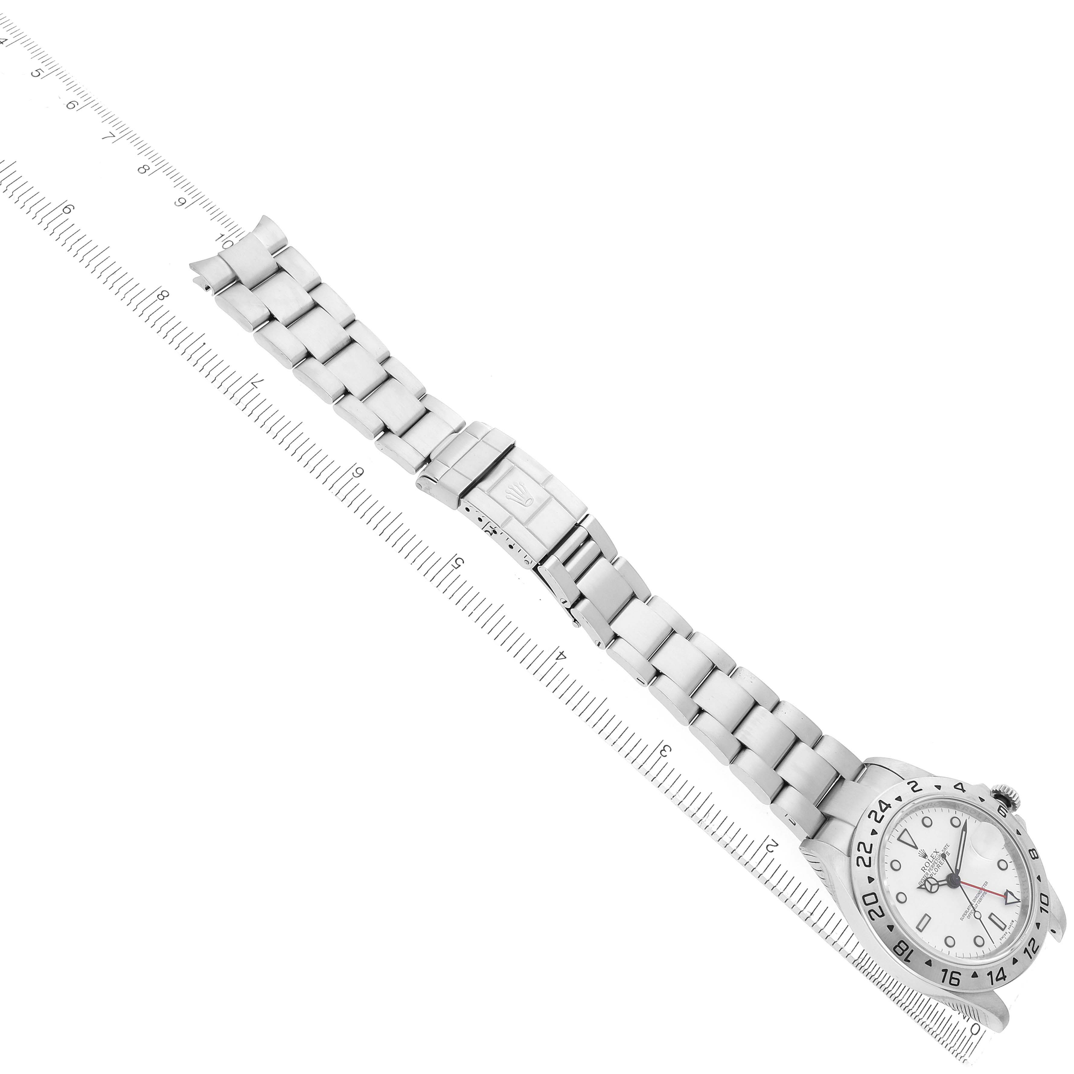 The image shows a Rolex Explorer 16570 Men
s Stainless Steel White Dial watch with a view of the dial, bezel, bracelet, and clasp laid next to a ruler.