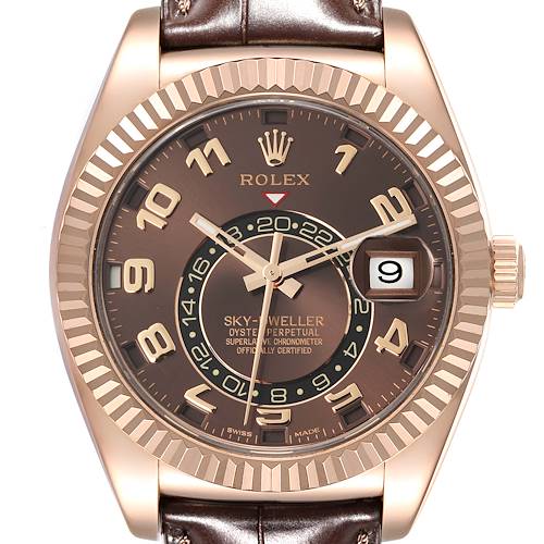 The image shows a Rolex Sky-Dweller watch face at a front angle, highlighting the brown dial, date window, and bezel.