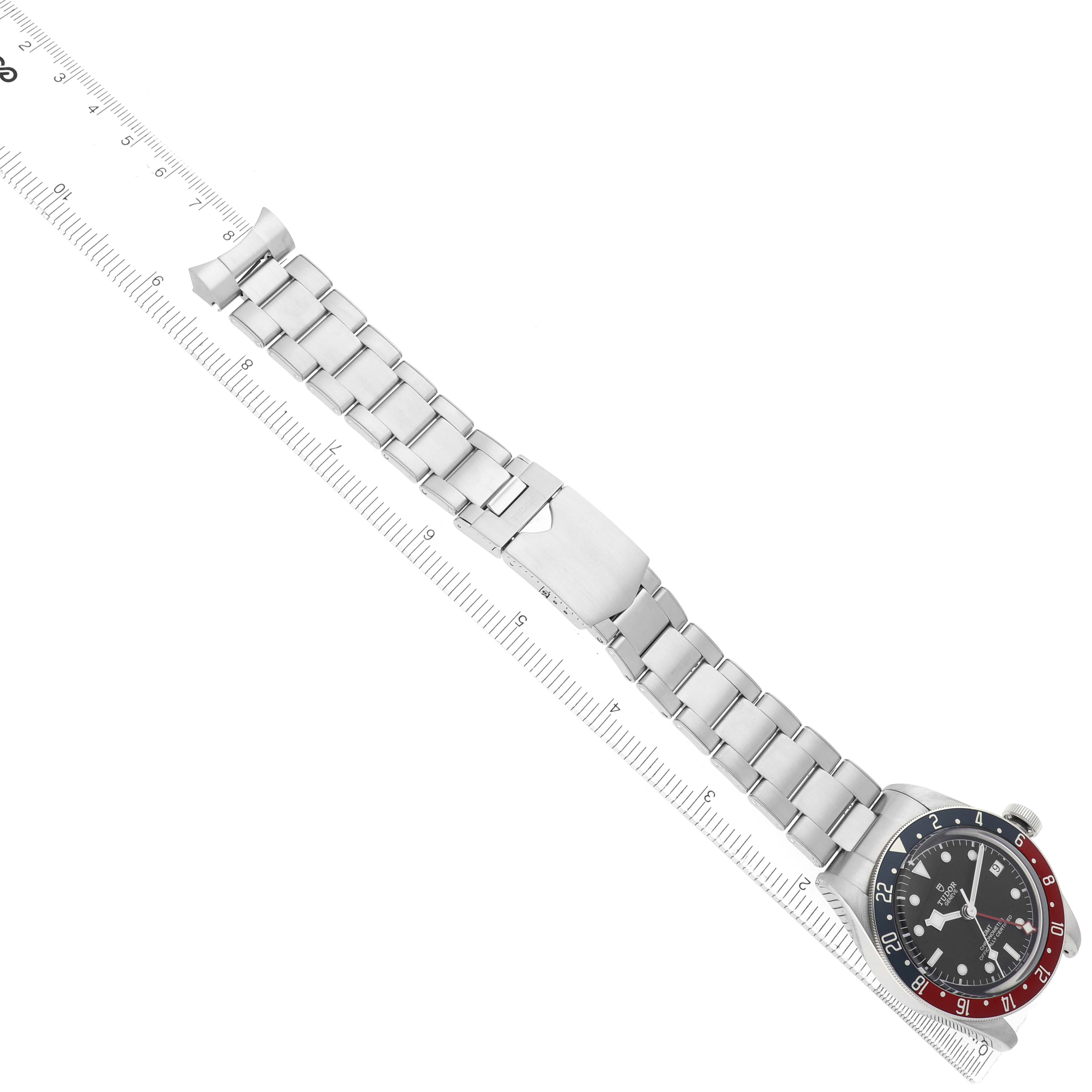 The Tudor Heritage Black Bay 79830RB Men
s Stainless Steel Black Dial watch is shown from an overhead angle, highlighting the bracelet and bezel across a ruler.