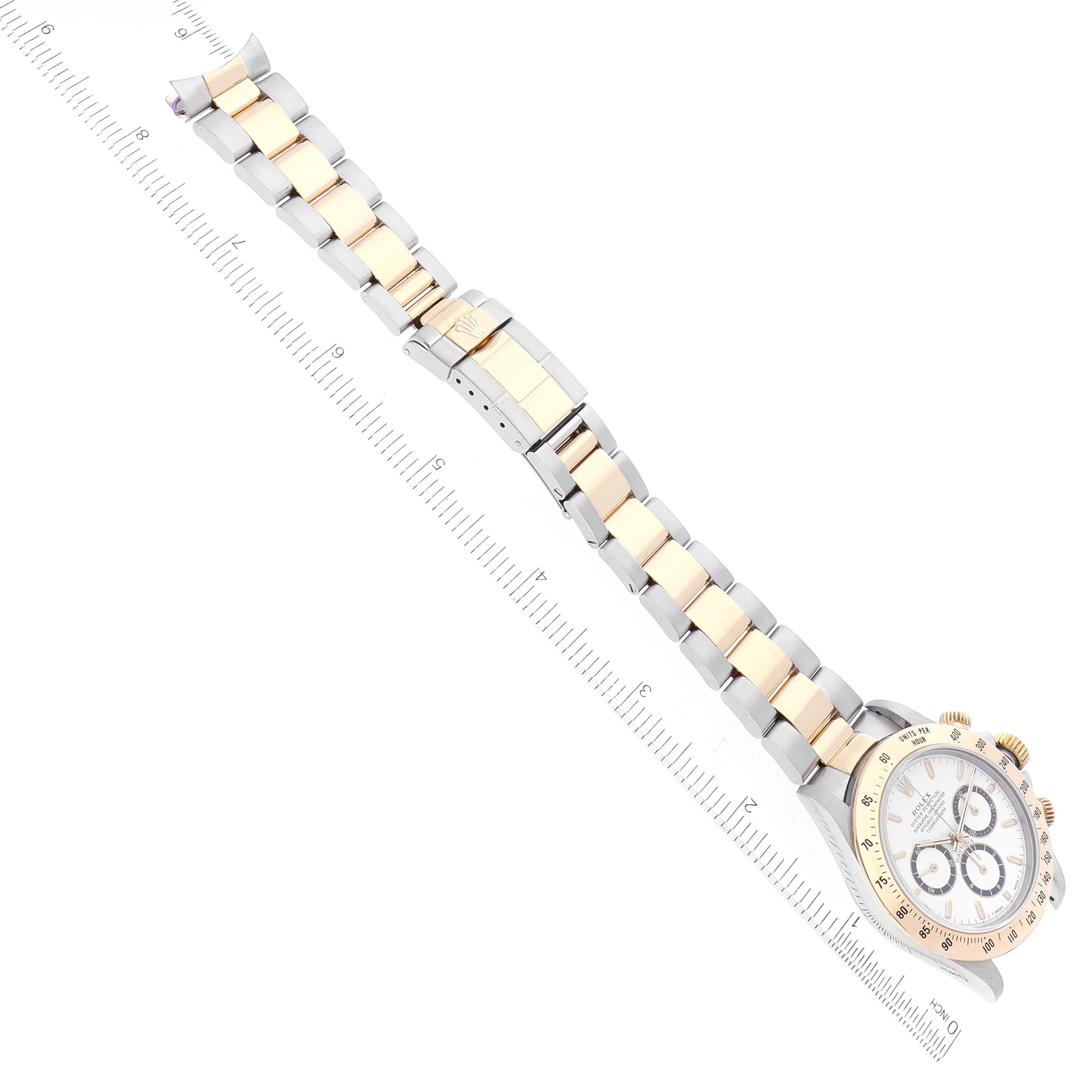 The image shows a Rolex Daytona 16523 Men's Steel and Gold (two tone) White Dial 16523 Men's Steel and Gold (two tone) White Dial watch at a slight diagonal angle, highlighting its bracelet and face, with a ruler for scale.