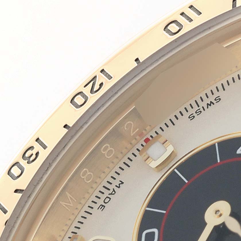 The image shows a close-up of the Rolex Daytona 116528 Men
s Yellow Gold Silver Dial
s bezel and part of the dial, featuring the tachymetric scale and some hour markers.