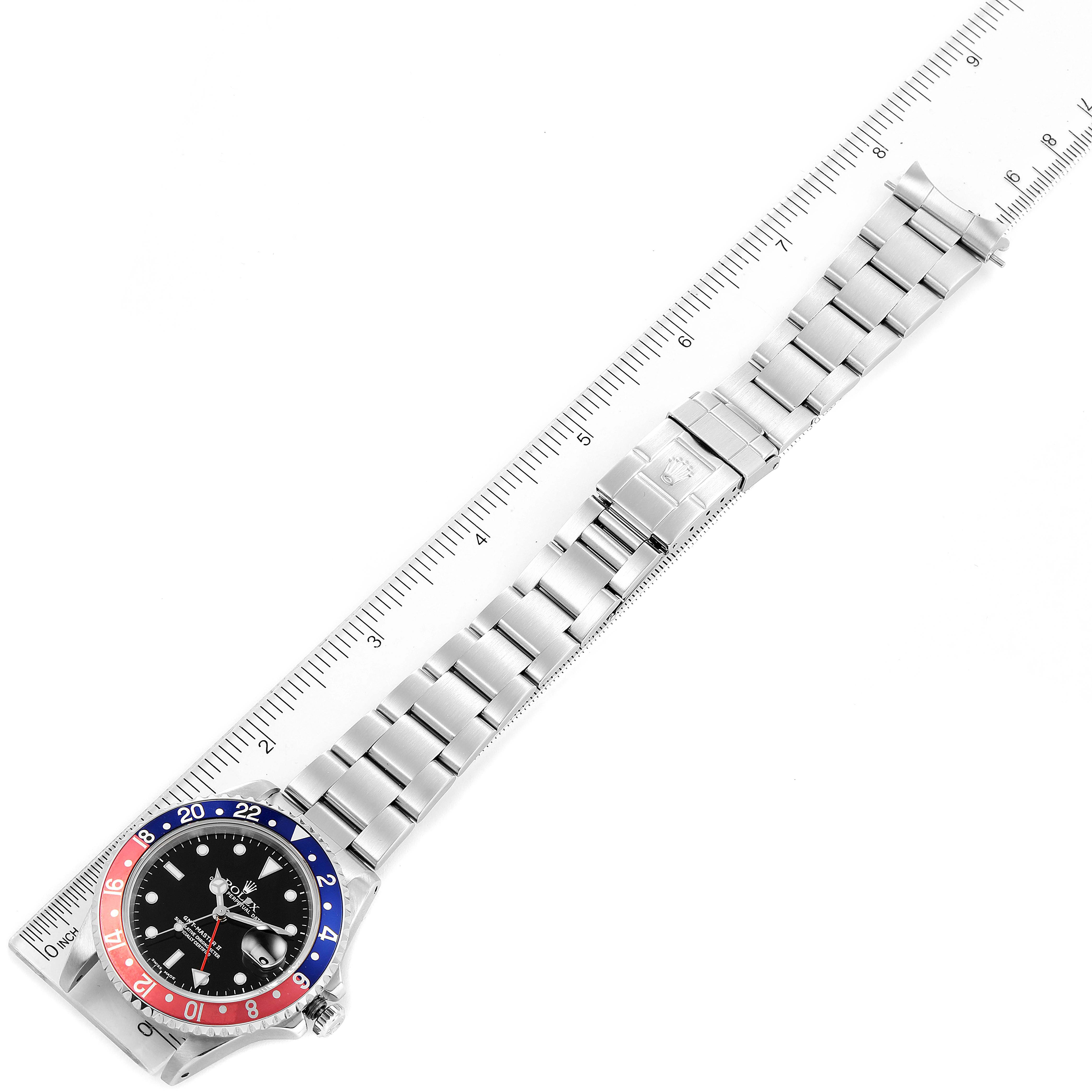 The image shows a top view of the Rolex GMT-Master 16710 Men
s Stainless Steel Black Dial 16710 Men
s Stainless Steel Black Dial watch alongside a ruler, displaying the bezel, dial, and bracelet.