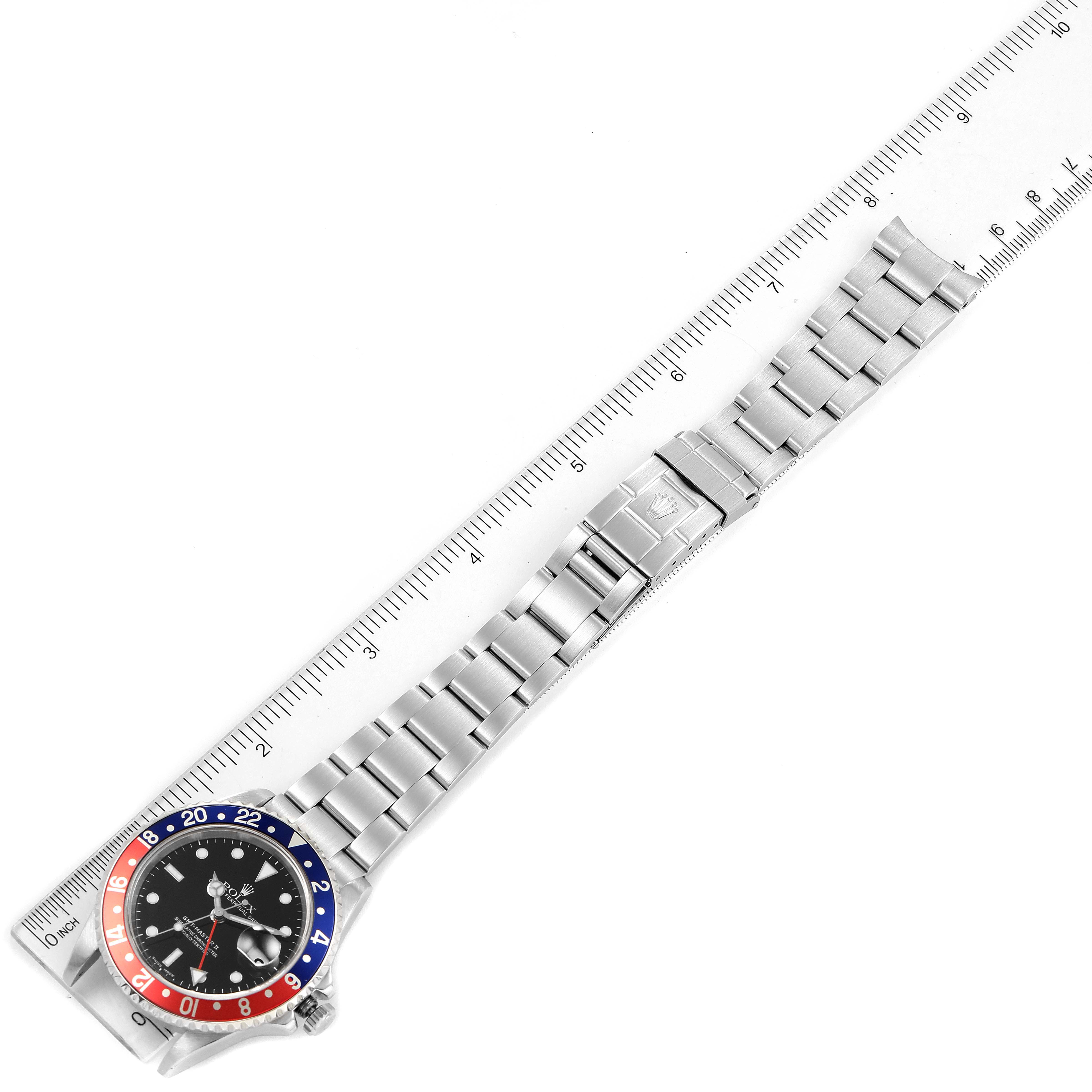 The image shows a top view of a Rolex GMT-Master 16710 Men
s Stainless Steel Black Dial 16710 Men
s Stainless Steel Black Dial watch, displaying the bezel, dial, and stainless steel bracelet against a ruler.