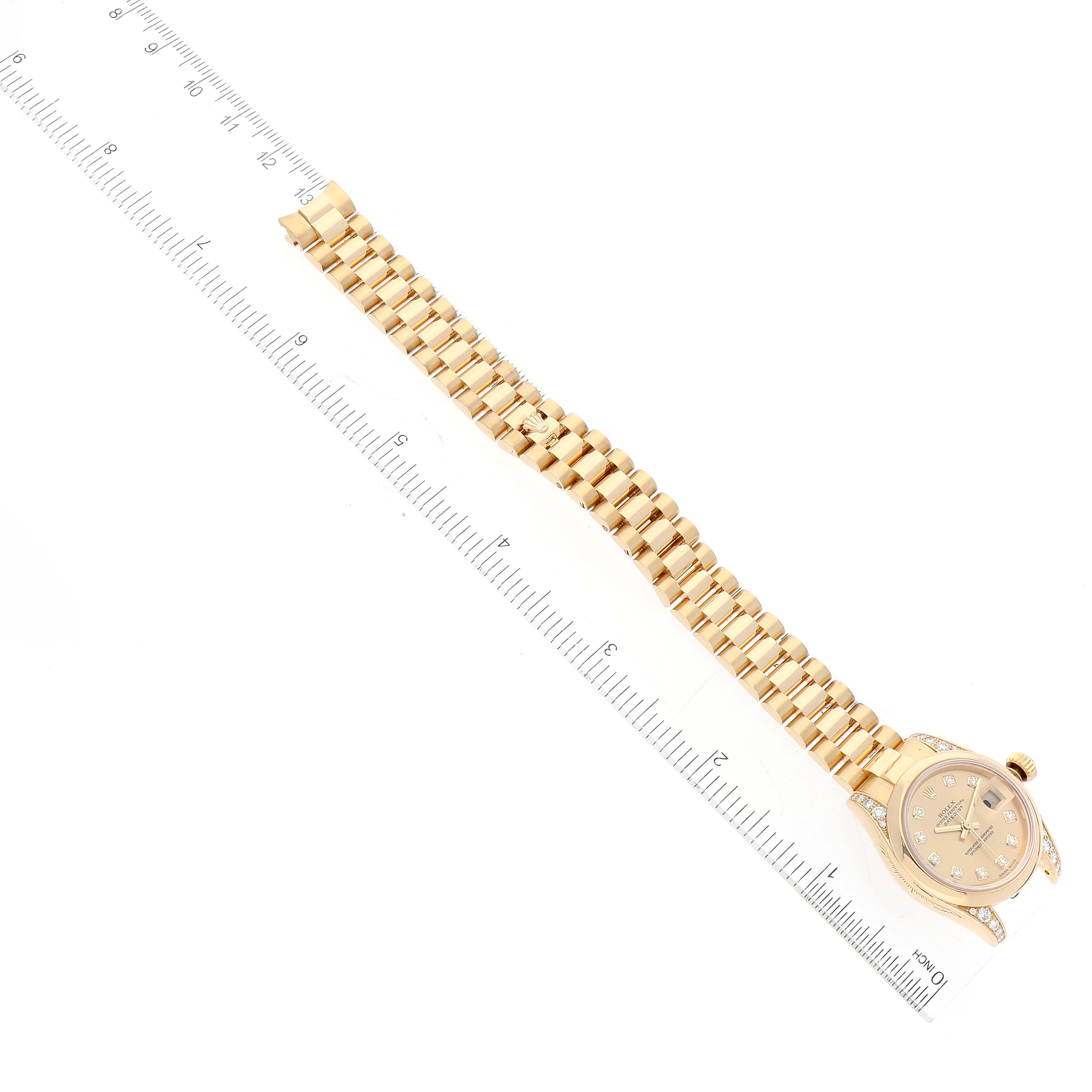 The image shows a Rolex President 179298 Women
s Yellow Gold Champagne Dial 179298 Women
s Yellow Gold Champagne Dial model watch laid flat alongside a ruler, displaying the watch
s face, band, and clasp.