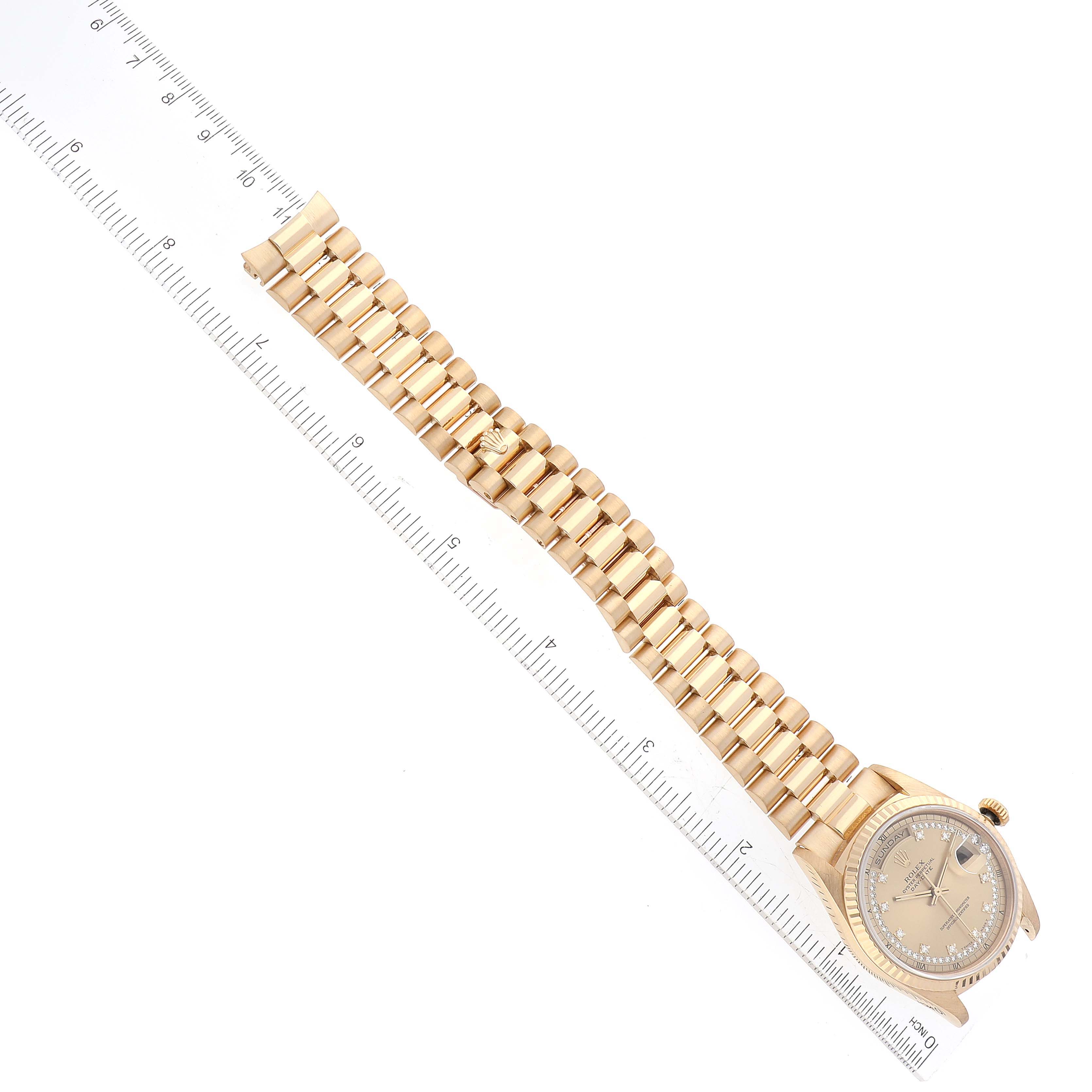 The image shows a top-down view of a Rolex President 18238 Men
s Yellow Gold Champagne Dial 18238 Men
s Yellow Gold Champagne Dial model watch with a metal band next to a ruler for scale.