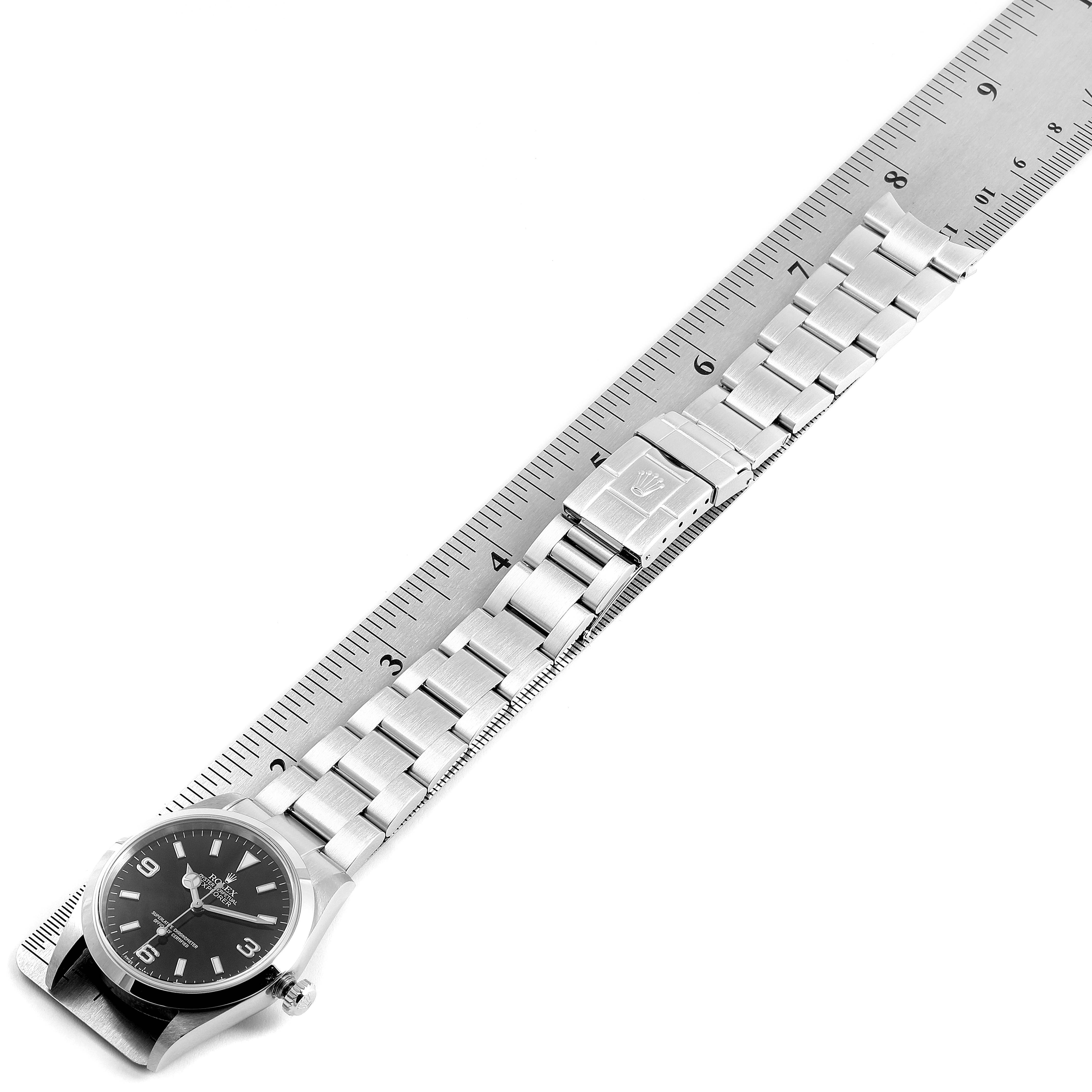The image shows the Rolex Explorer 14270 Men
s Stainless Steel Black Dial 14270 Men
s Stainless Steel Black Dial watch, laid flat with a metal ruler, displaying the face and bracelet with clasp.