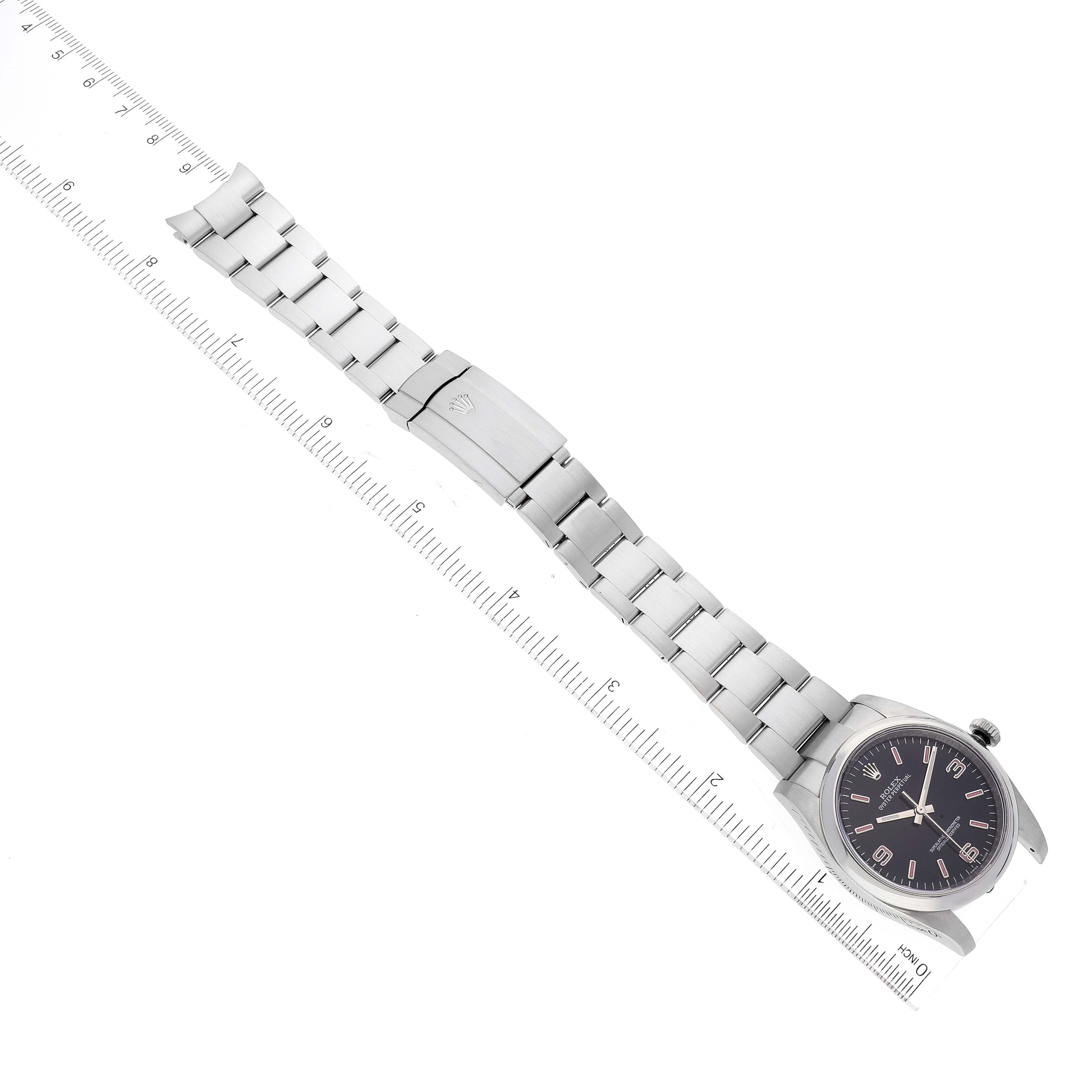 The image shows a top-down view of a Rolex Oyster Perpetual 116000 Men's Stainless Steel Black Dial 116000 Men's Stainless Steel Black Dial watch, highlighting its bracelet, clasp, and face placed alongside a ruler for scale.
