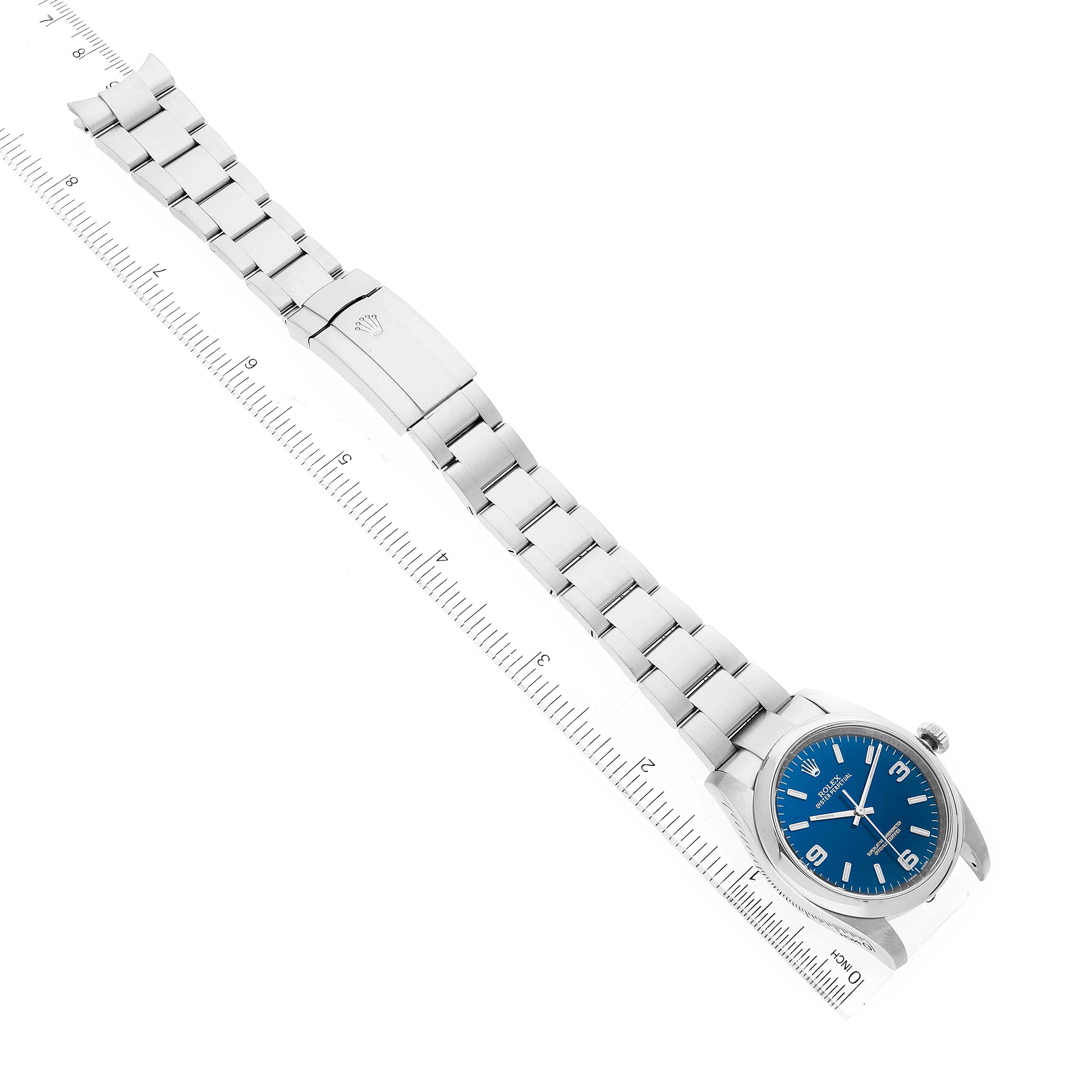 The image shows a full view of the Rolex Oyster Perpetual 116000 Men's Stainless Steel Blue Dial 116000 Men's Stainless Steel Blue Dial watch, displaying its blue dial, metal bracelet, and clasp next to a ruler.