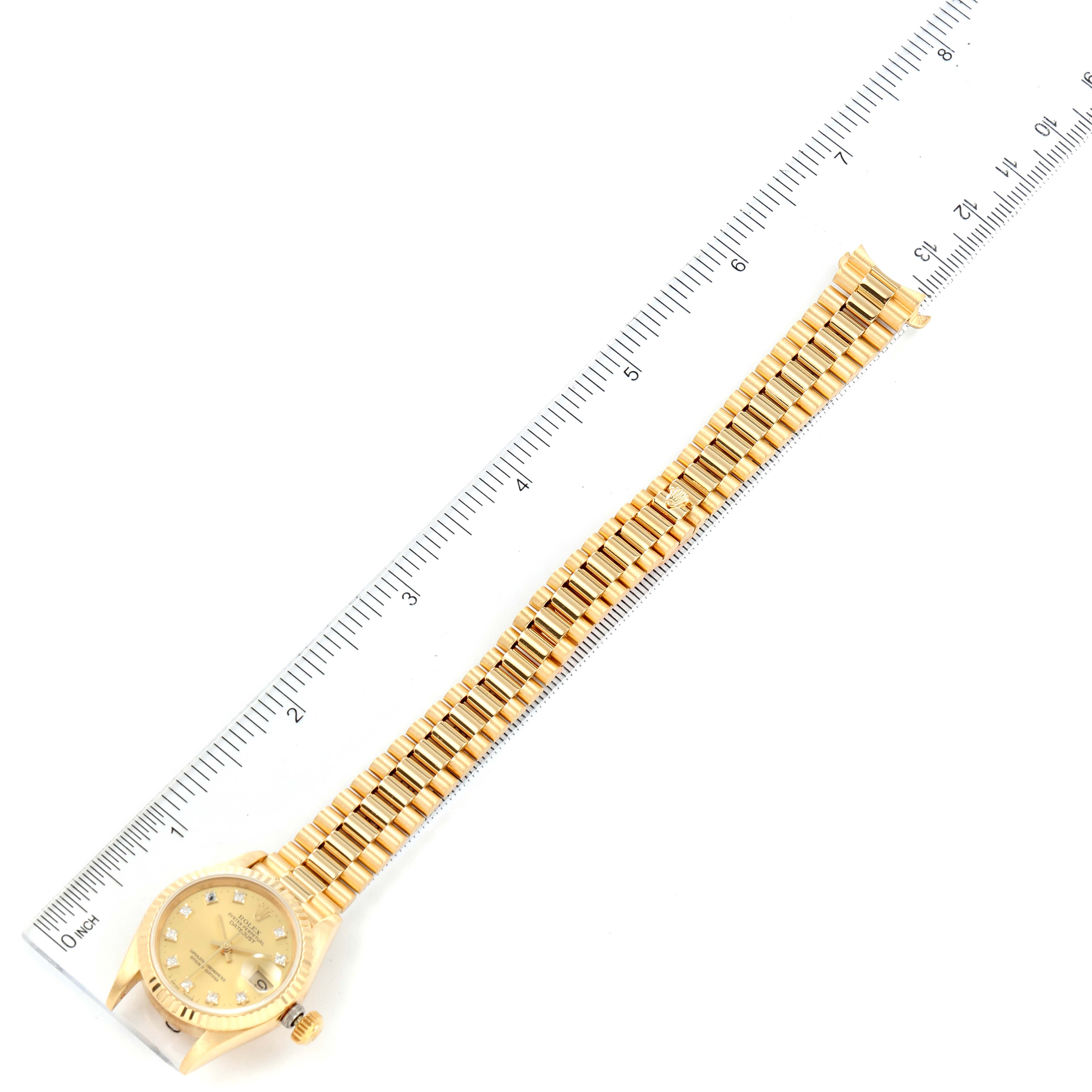 The image shows a top view of a Rolex President 69178 Women
s Yellow Gold Champagne Dial 69178 Women
s Yellow Gold Champagne Dial model watch, including its face and whole bracelet next to a ruler for measurement.