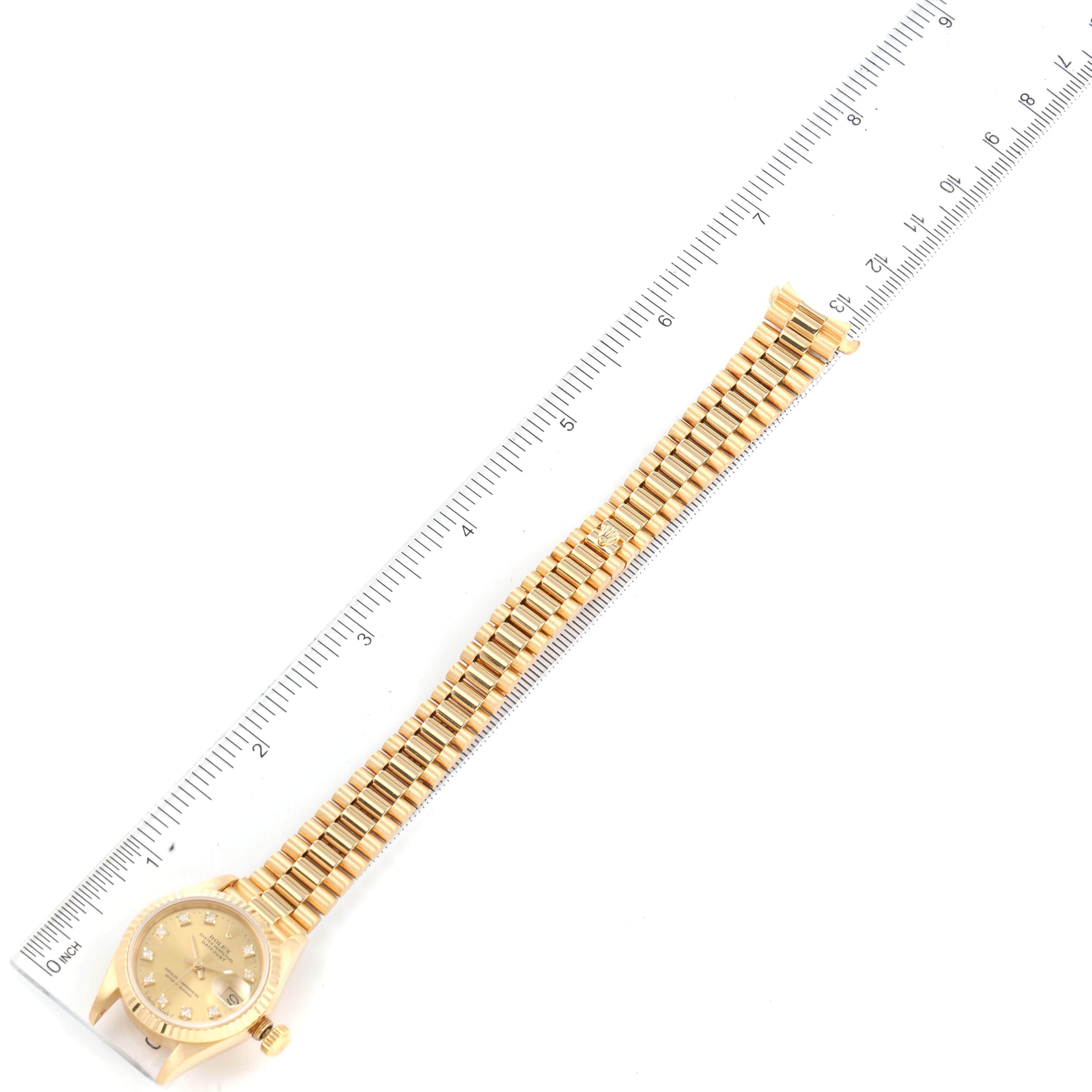 This image shows a Rolex President 69178 Women
s Yellow Gold Champagne Dial 69178 Women
s Yellow Gold Champagne Dial watch displayed flat with the full length of its bracelet and dial visible alongside a ruler.