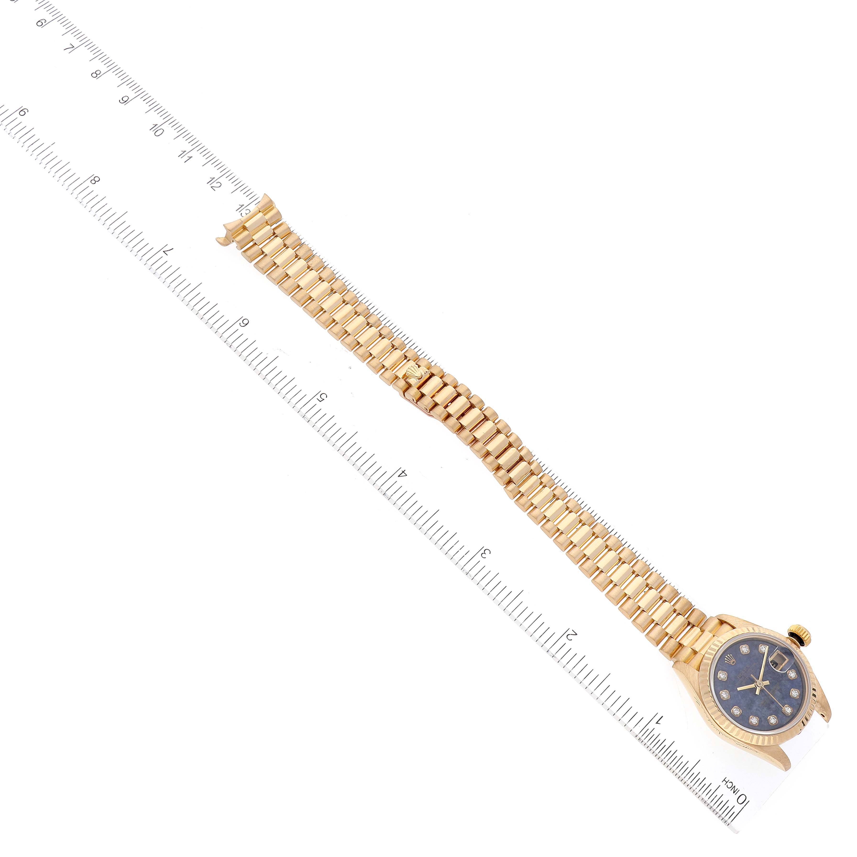 The image shows a Rolex President 69178 Women's Yellow Gold Blue Dial 69178 Women's Yellow Gold Blue Dial model watch laid flat next to a ruler, displaying the blue dial and gold bracelet at an angled view.