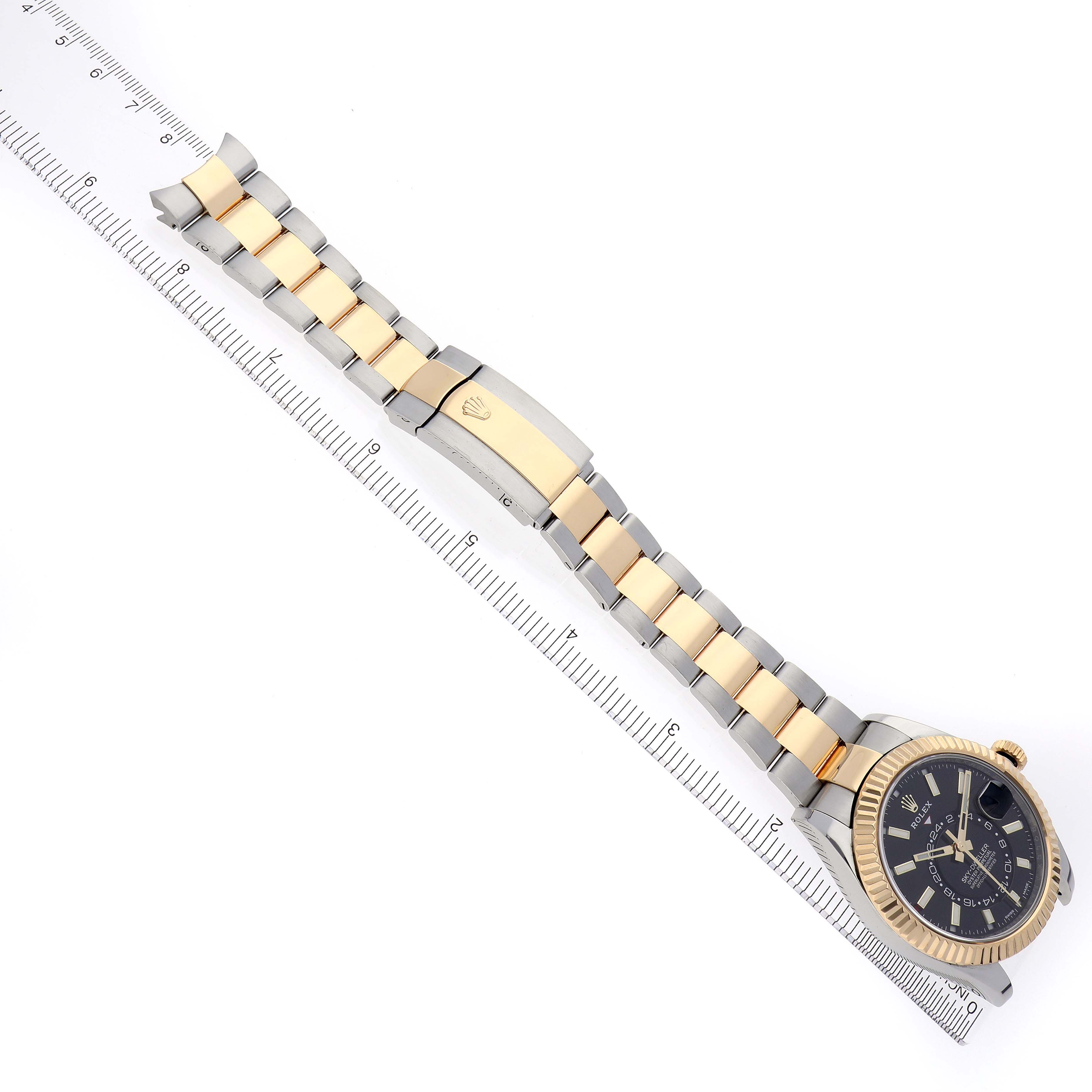 The image shows a Rolex Sky-Dweller 326933 Men
s Steel and Gold (two tone) Black Dial 326933 Men
s Steel and Gold (two tone) Black Dial watch placed flat with an extended two-tone bracelet against a ruler for scale.