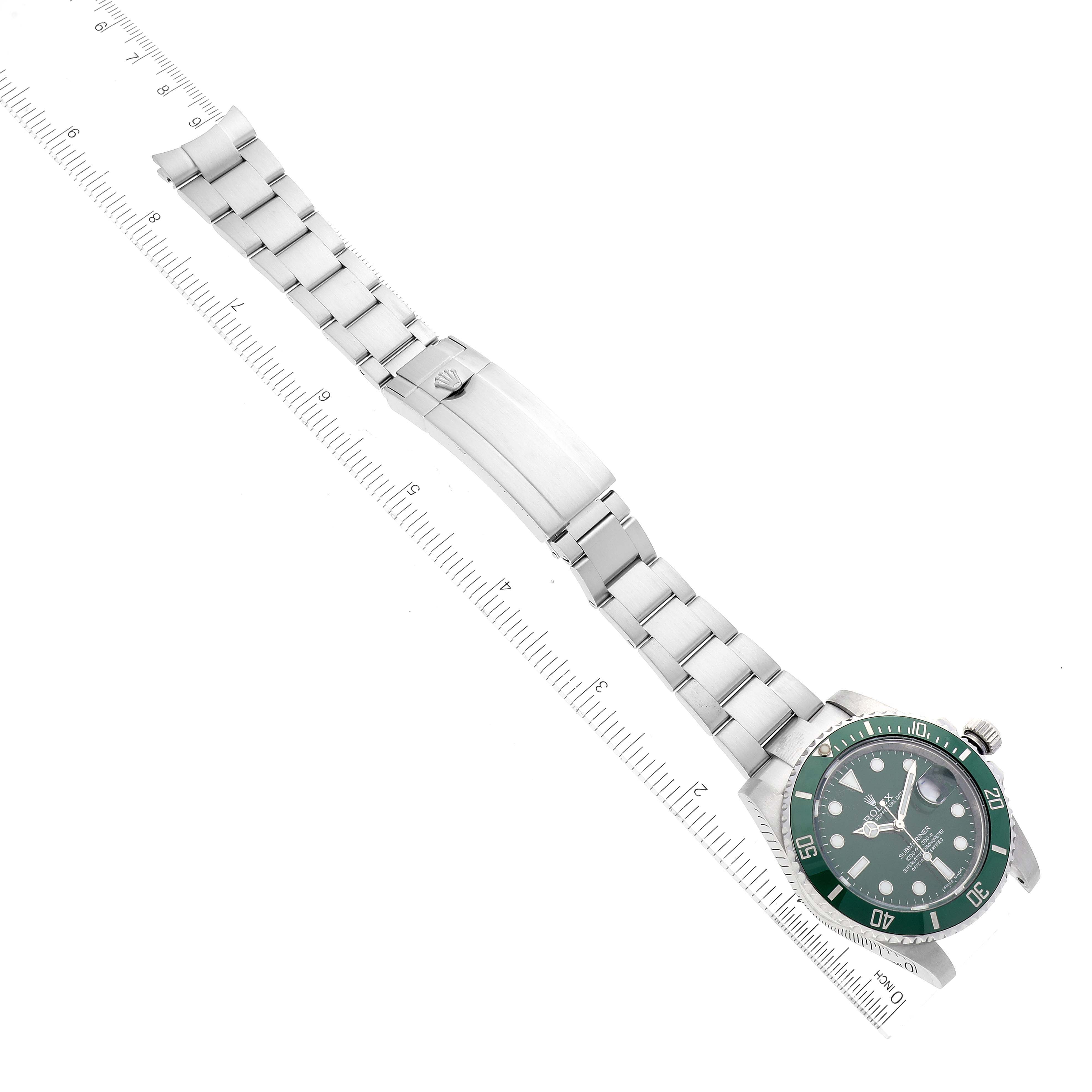The image shows a Rolex Submariner 116610LV Men
s Stainless Steel Green Dial 116610LV Men
s Stainless Steel Green Dial watch flat, with the face, bracelet, and clasp, alongside measuring rulers.