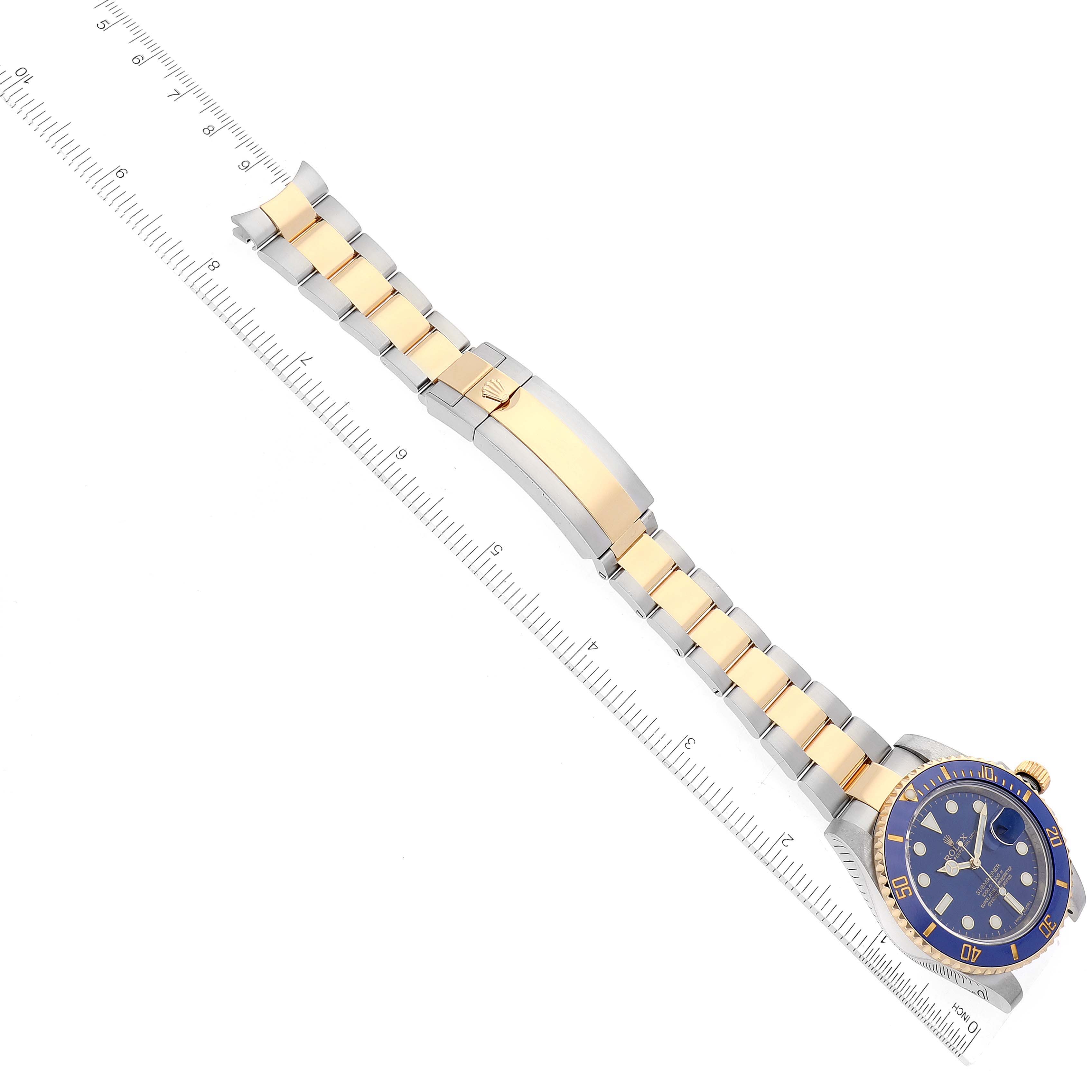 The image shows a top view of a Rolex Submariner 116613 Men's Steel and Gold (two tone) Blue Dial 116613 Men's Steel and Gold (two tone) Blue Dial watch displaying the watch face, band, and clasp, alongside a ruler for scale.