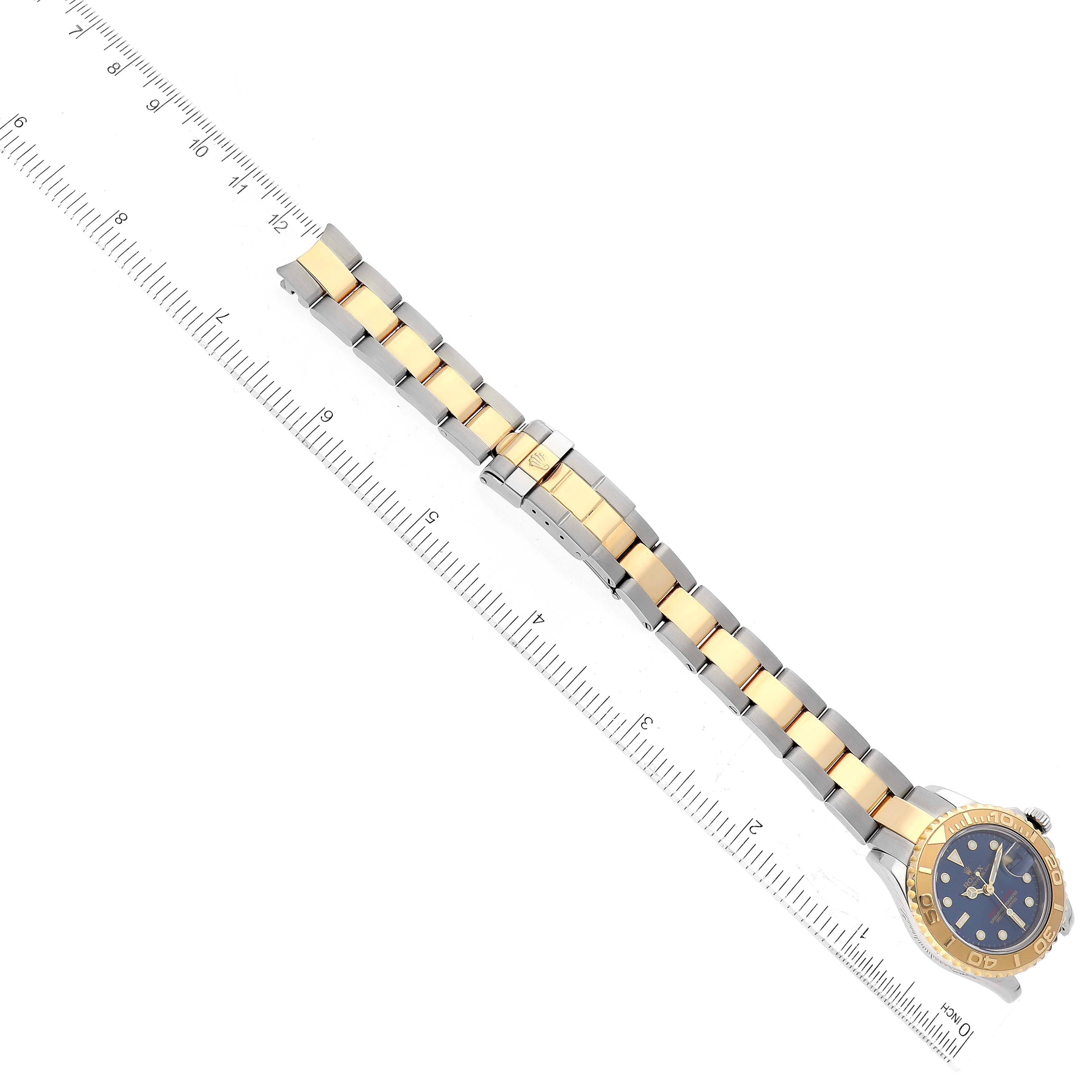 The image shows a top view of the Rolex Yacht-Master 169623 Women's Steel and Gold (two tone) Blue Dial 169623 Women's Steel and Gold (two tone) Blue Dial watch, displaying its band, face, and bezel alongside a ruler for scale.